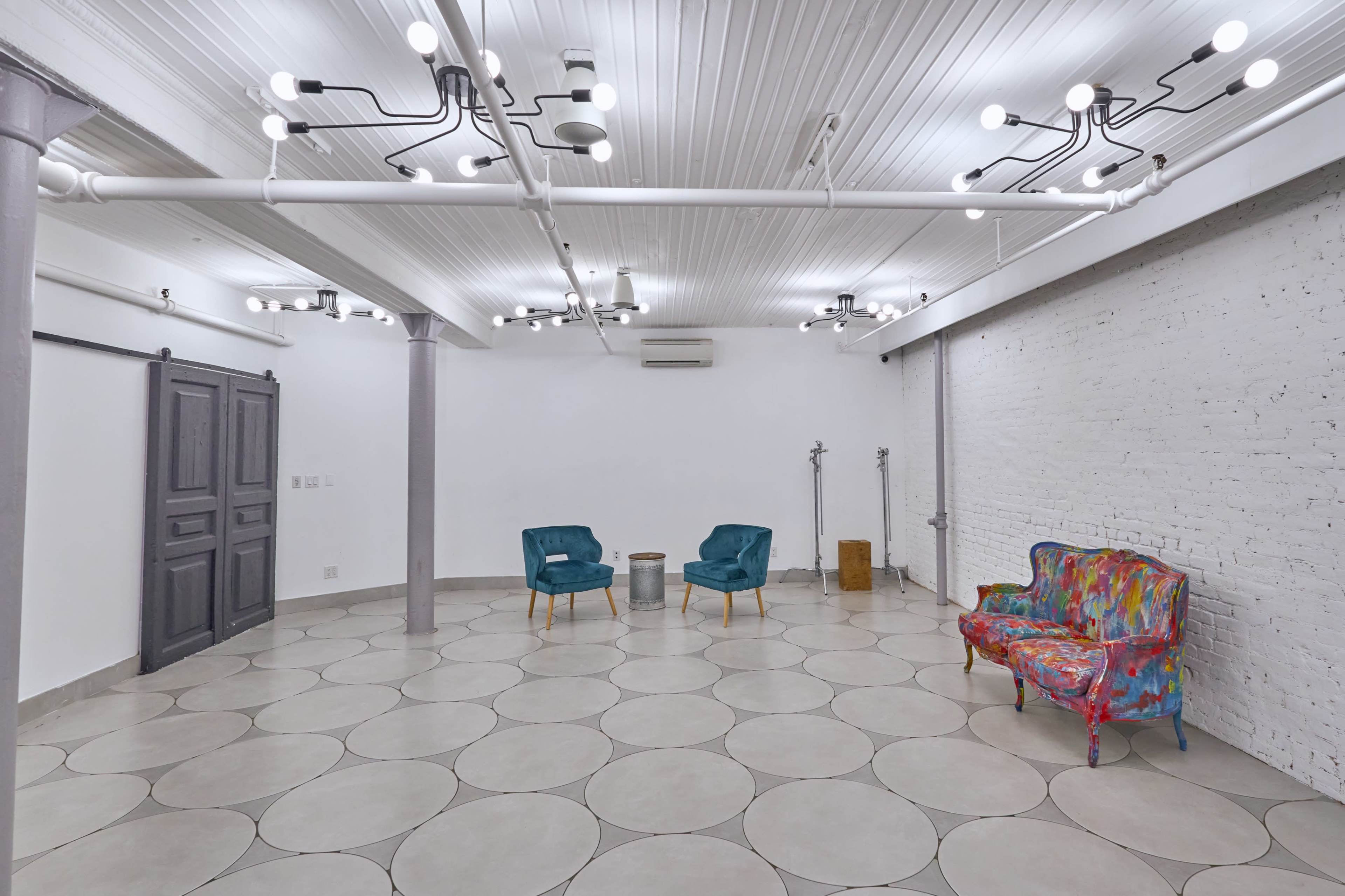 The image shows a modern, empty room with gray tiled flooring, white walls, and colorful furnishings including a vibrant couch and two blue chairs.