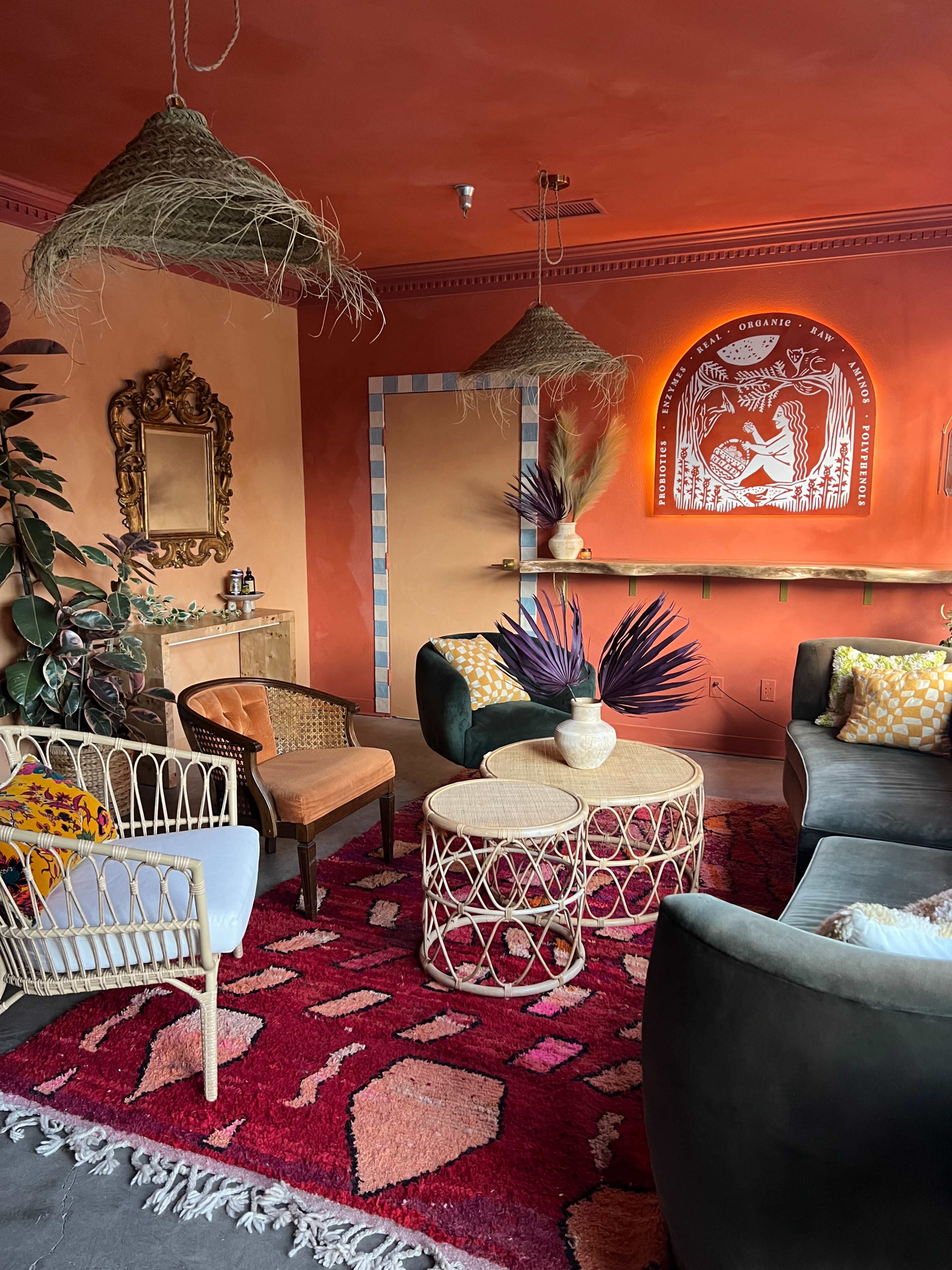 The scene depicts a cozy indoor lounge featuring earthy-toned walls, eclectic seating arrangements, decorative lighting, and vibrant textile accents.