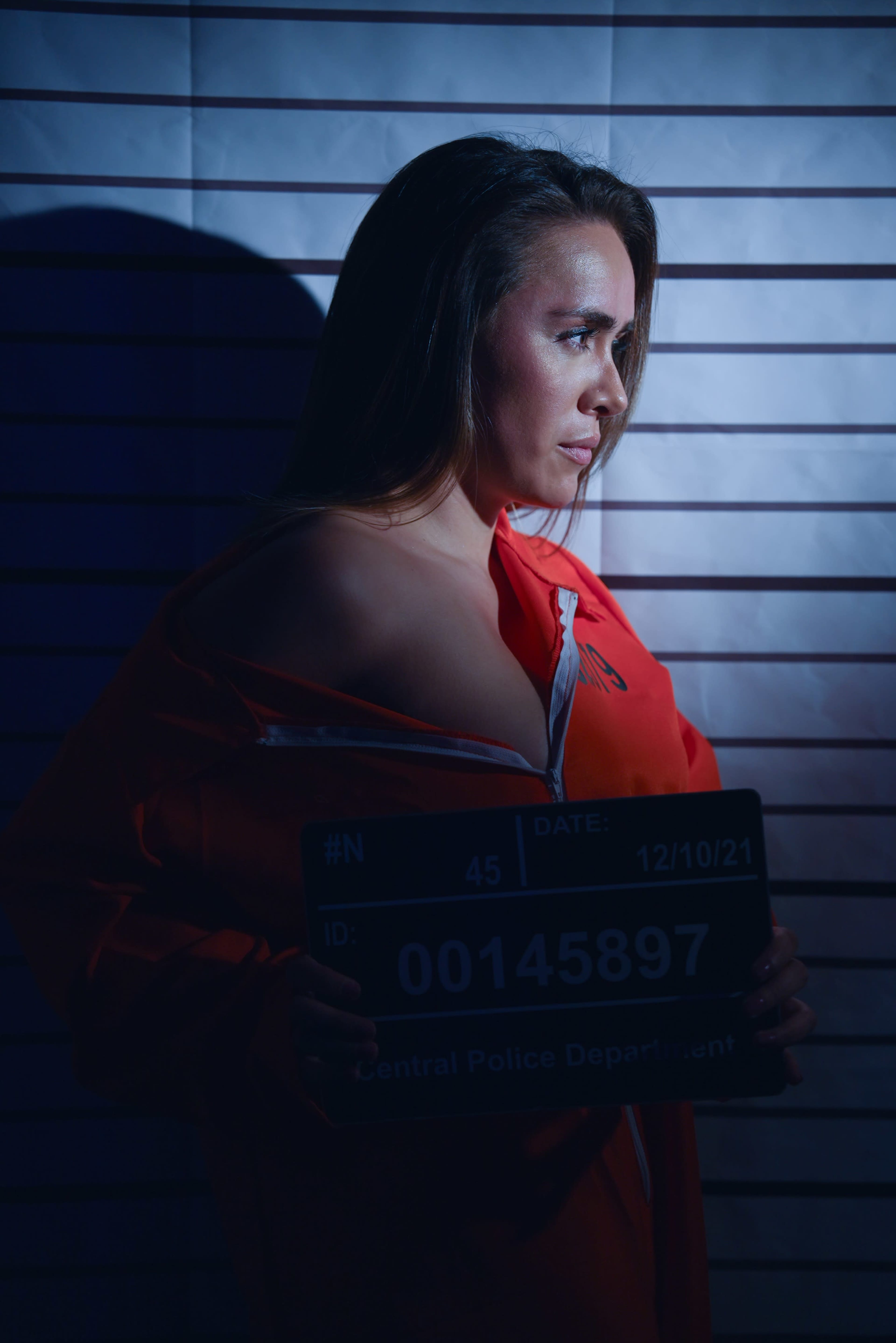 A woman in an orange prison jumpsuit holds a police identification sign against a backdrop of height measurement lines.