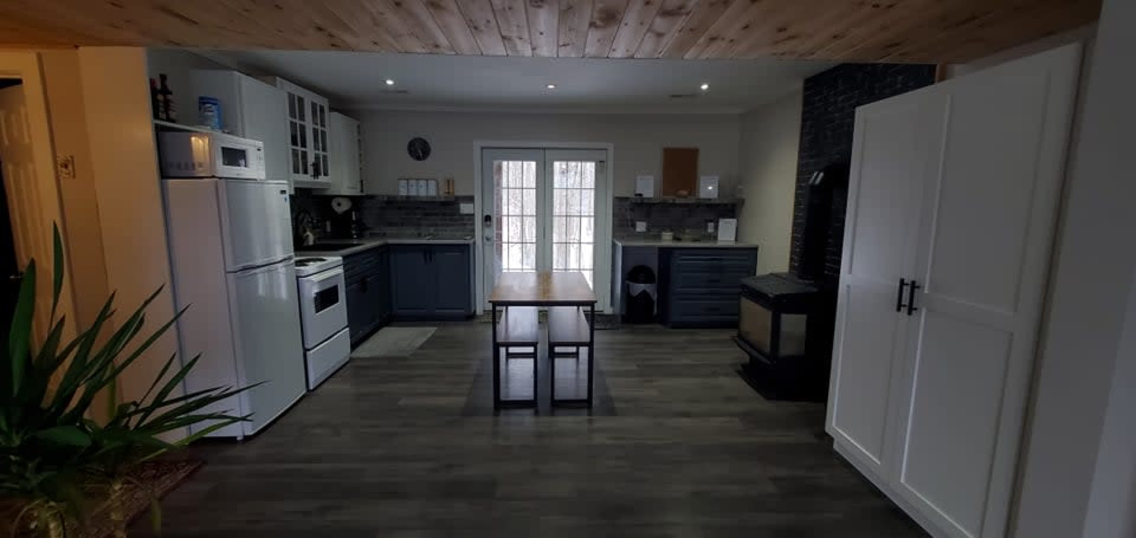 A spacious kitchen features a central table, white cabinets, a dark stove, and large windows leading to an outdoor area.