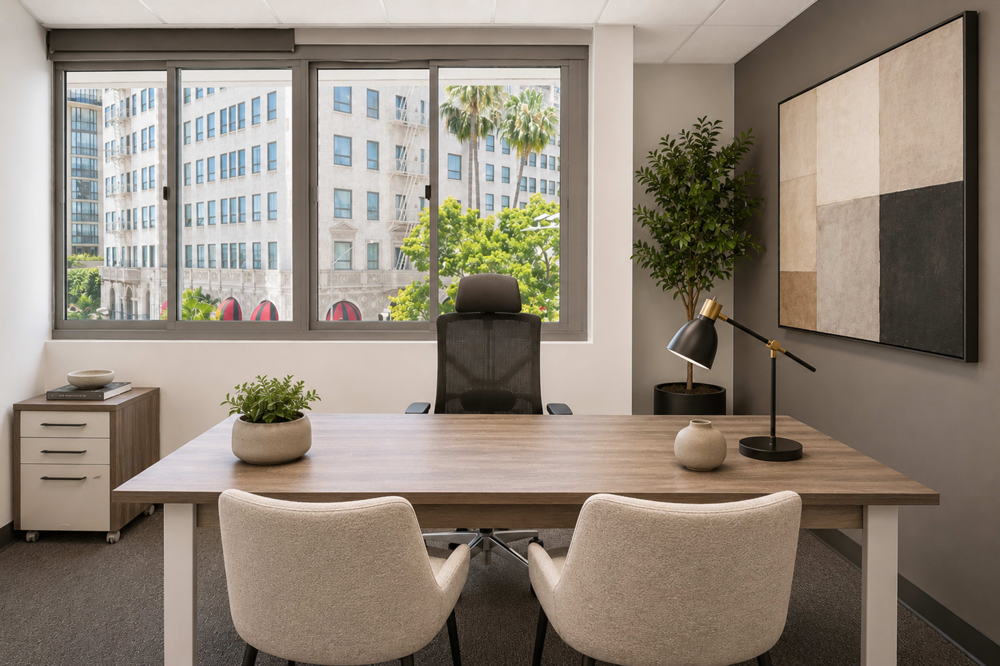 The image shows a modern office with a wooden desk, two chairs, a lamp, and large windows overlooking a cityscape featuring tall buildings and palm trees.