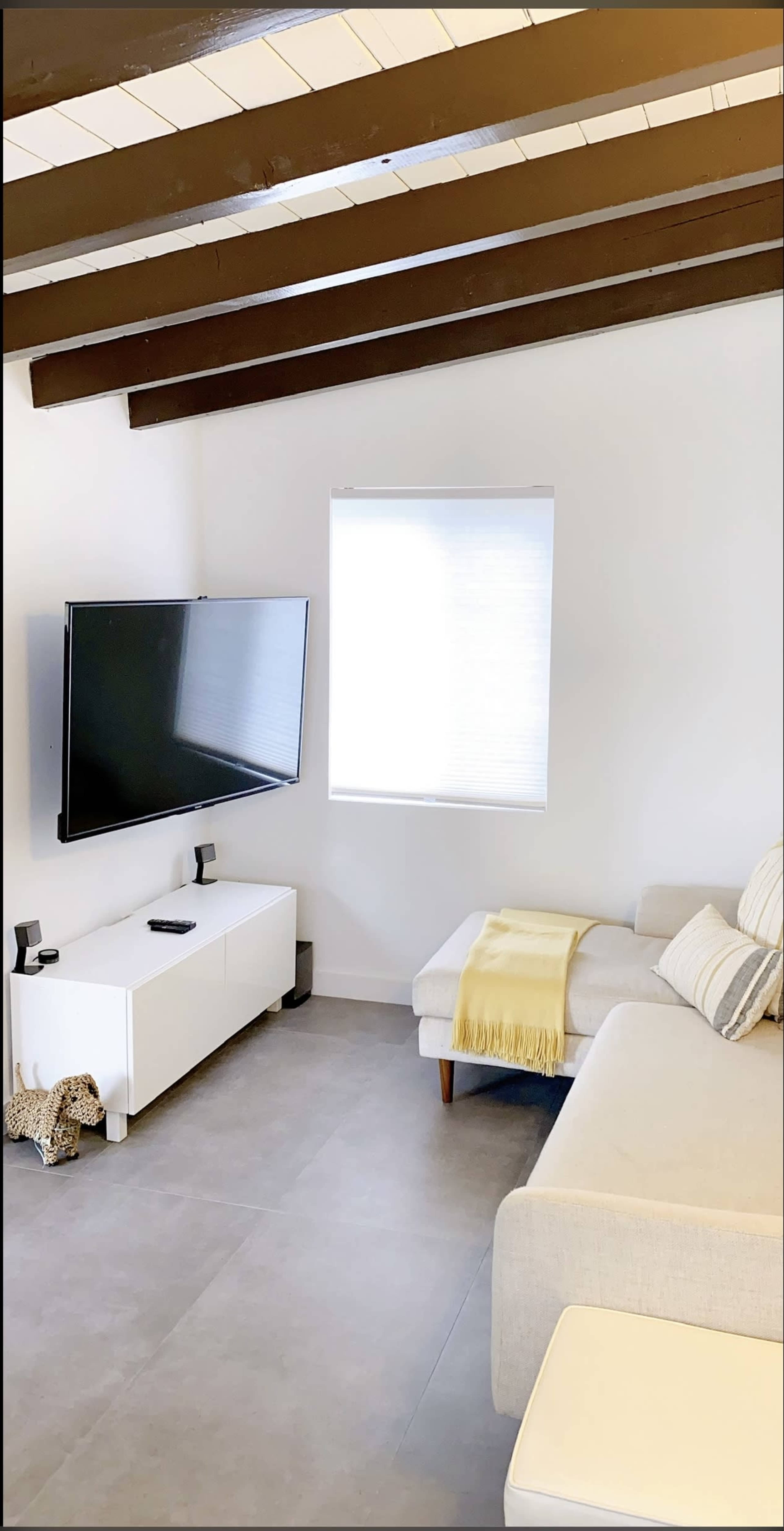 A modern living room with a television mounted on the wall, a light-colored sectional sofa, and a white media console.