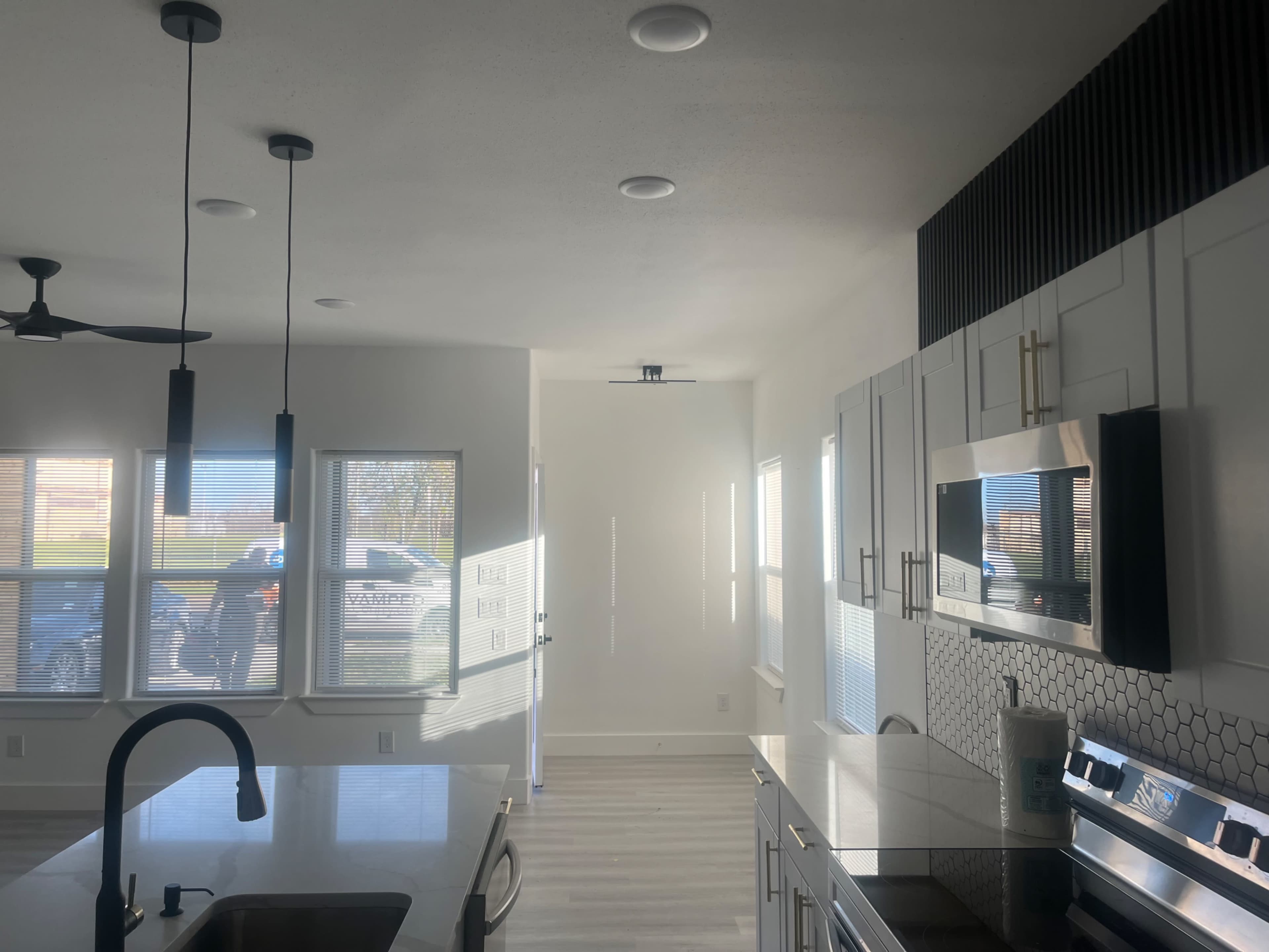 The image shows a modern kitchen with a large island, a microwave, and a sleek design, illuminated by natural light streaming through multiple windows.