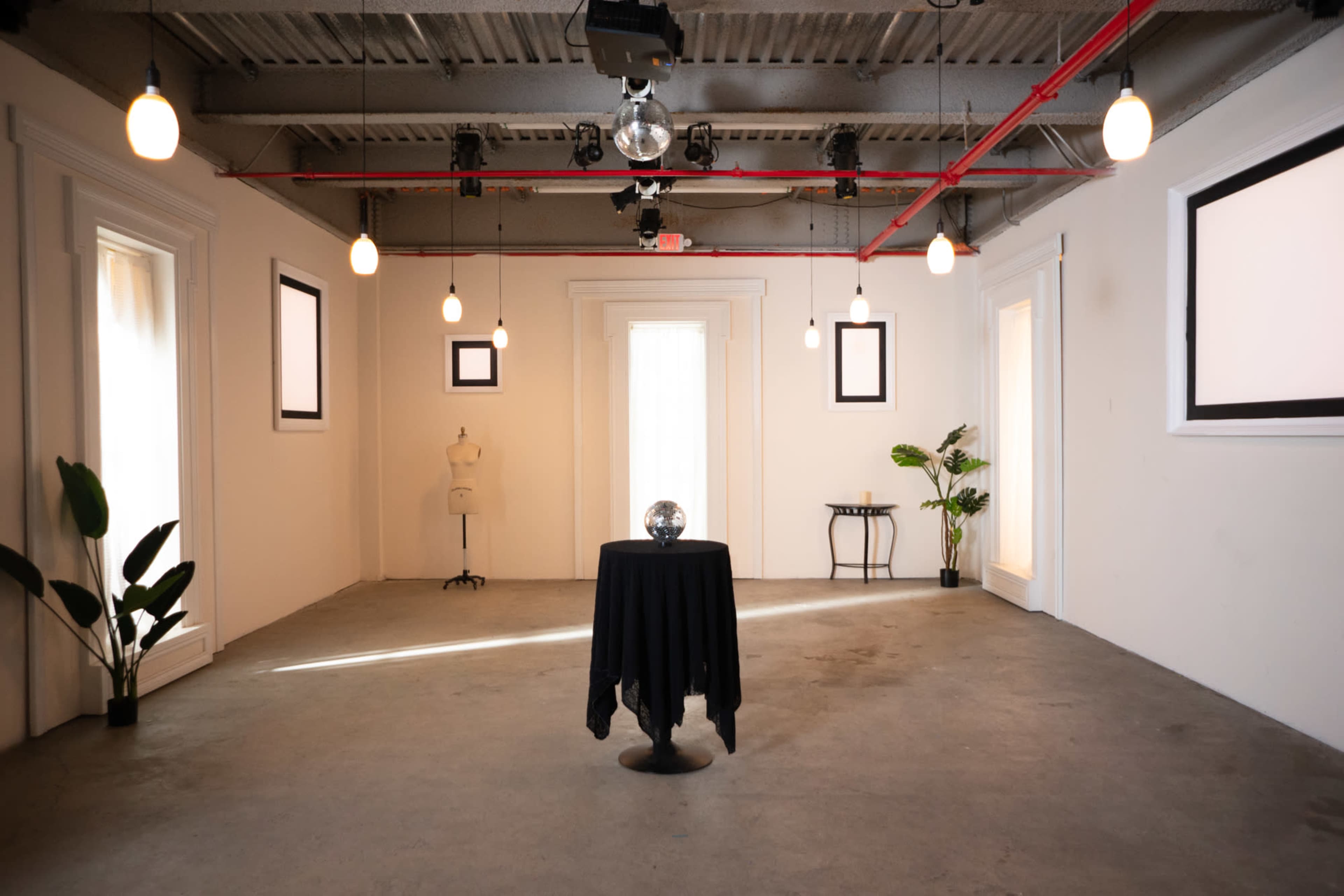 The room features a round table covered with a black cloth, a disco ball on top, and is surrounded by minimalist decor, including plants and framed wall art.