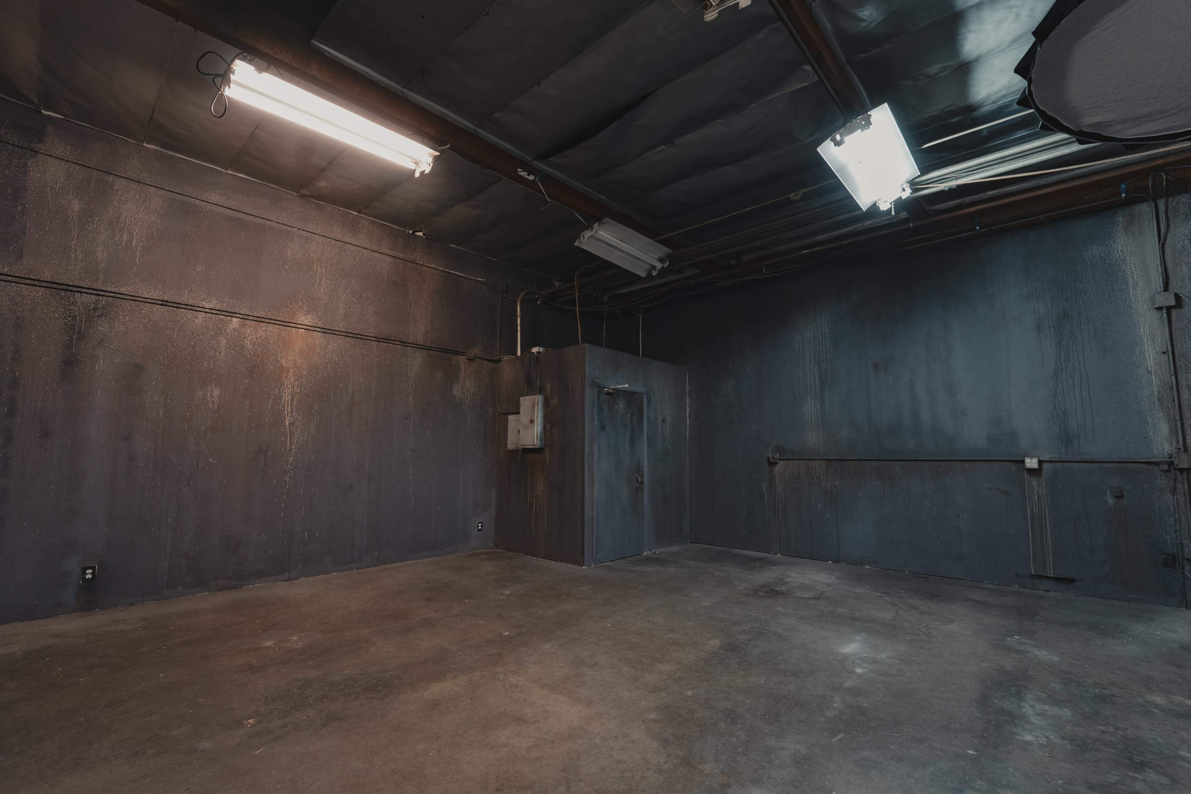 A dimly lit industrial room with dark, textured walls and a concrete floor.