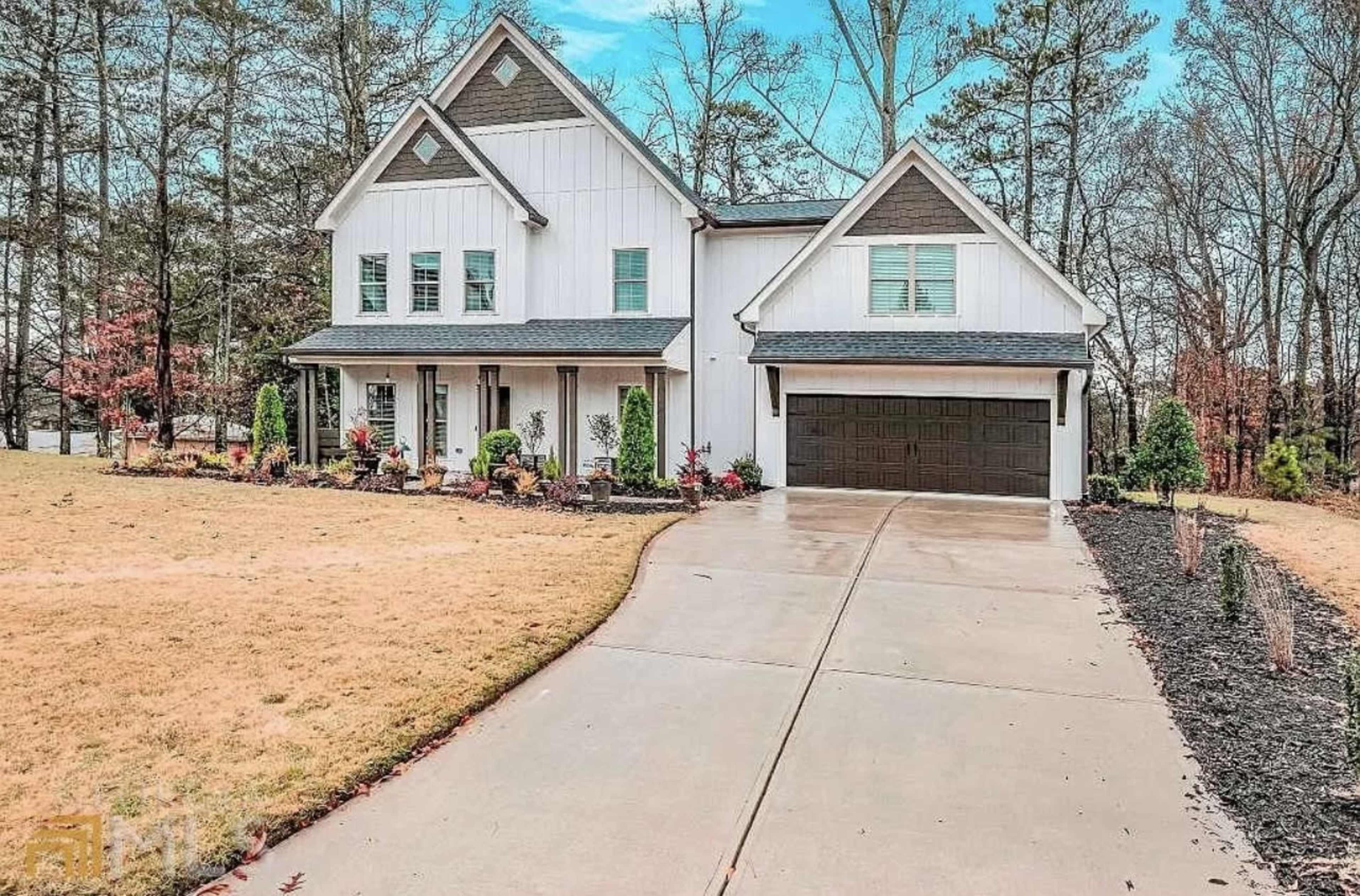 A white two-story house with a gray roof features a spacious driveway and landscaped front yard.