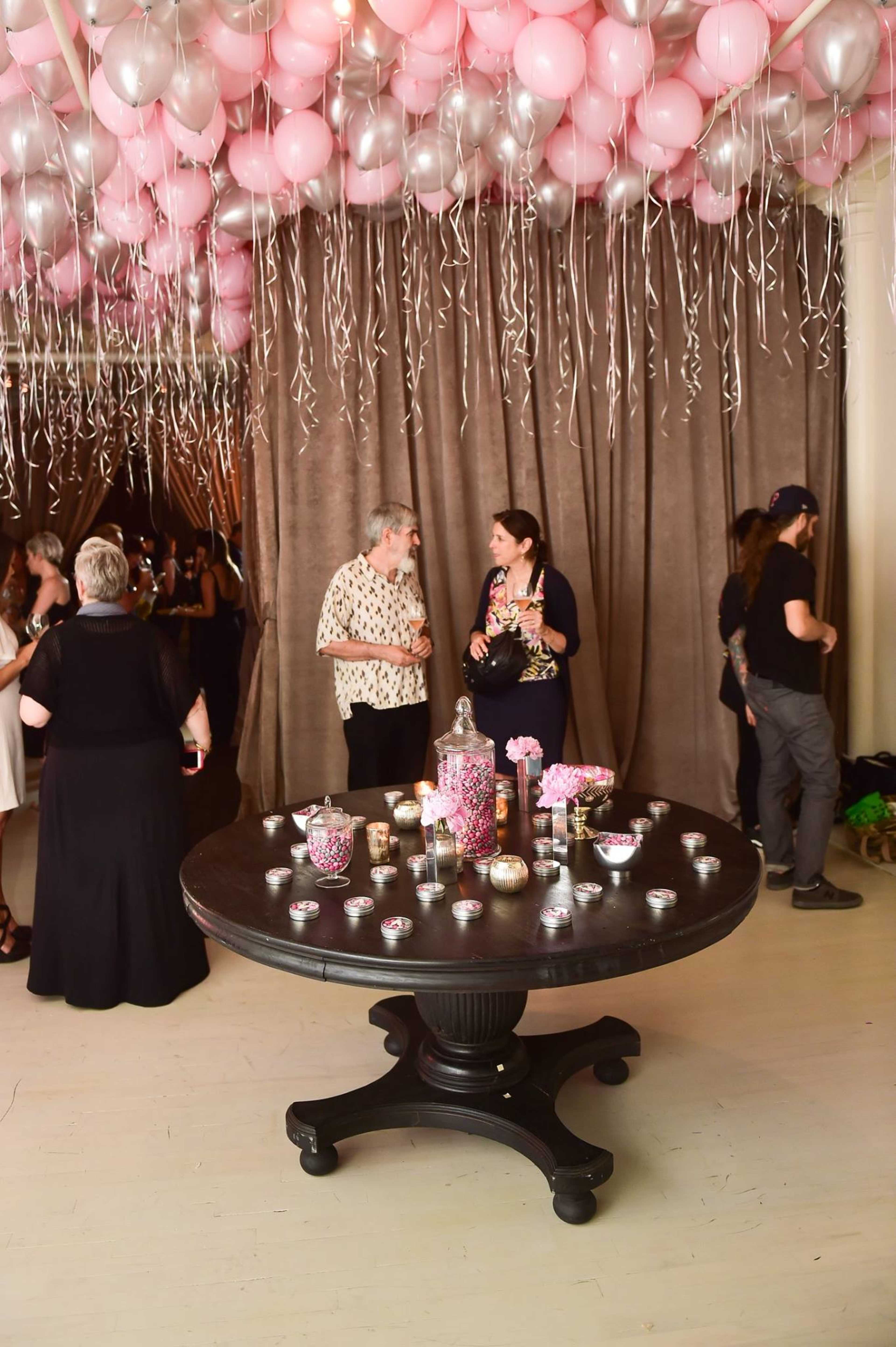 A black table covered with various decorative items sits in a room with a ceiling adorned with pink balloons and glittering streamers.