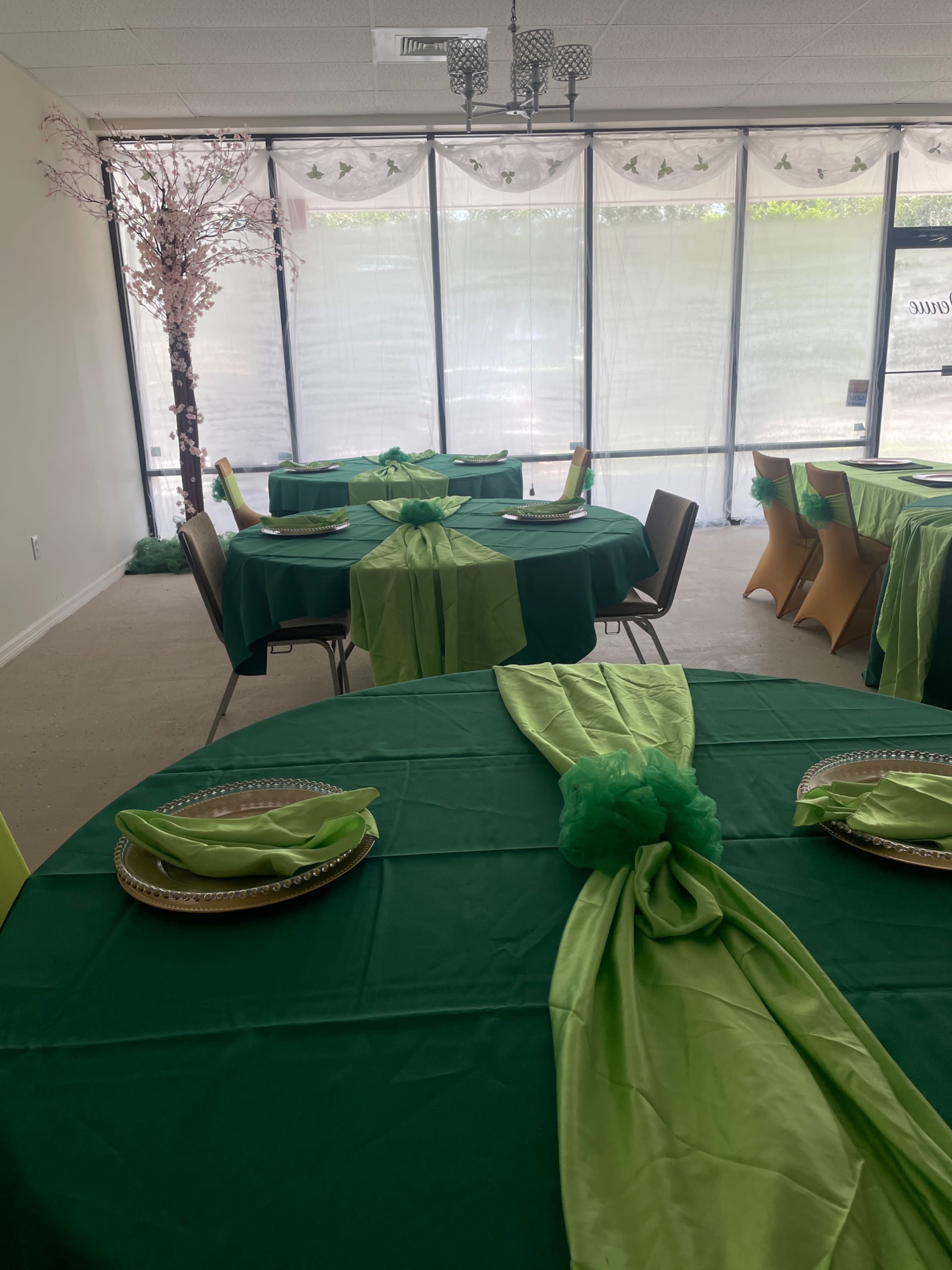 A banquet hall set up with green tables covered in matching tablecloths and arranged with neatly folded napkins.