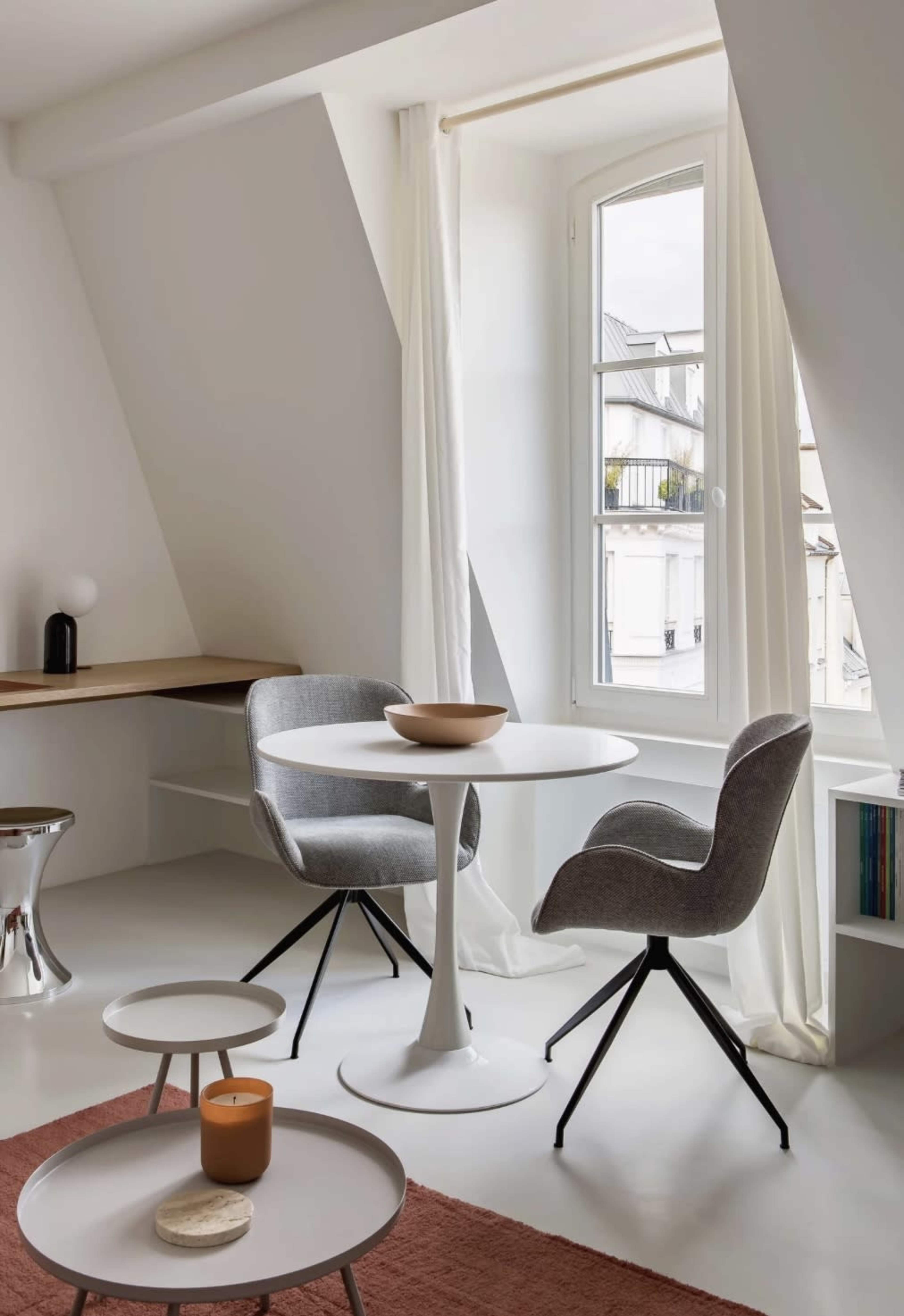 A modern interior features two gray chairs at a round white table near a window, complemented by a soft rug and decorative items.