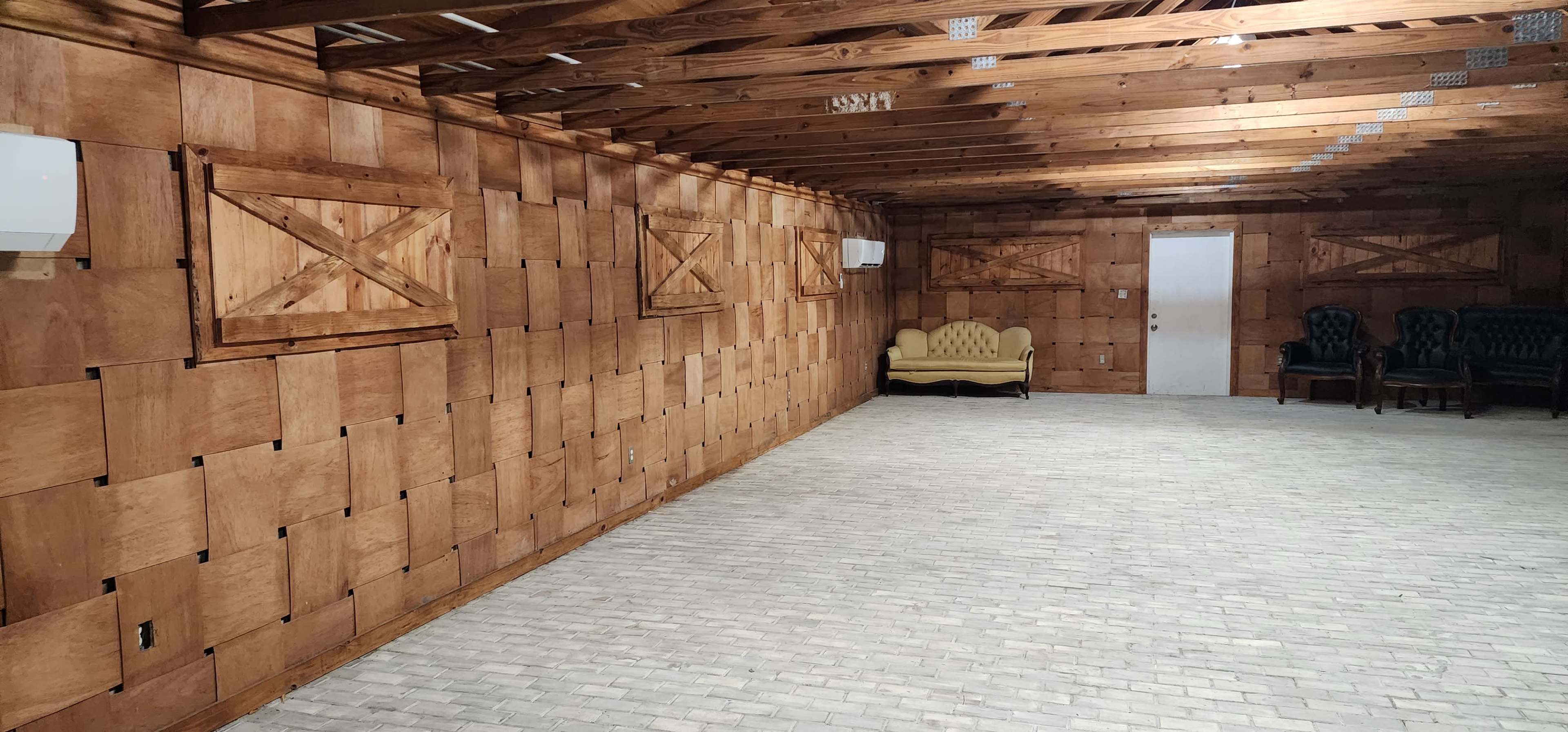 An empty room with wooden walls, a brick floor, a yellow couch, and two dark chairs against the far wall.