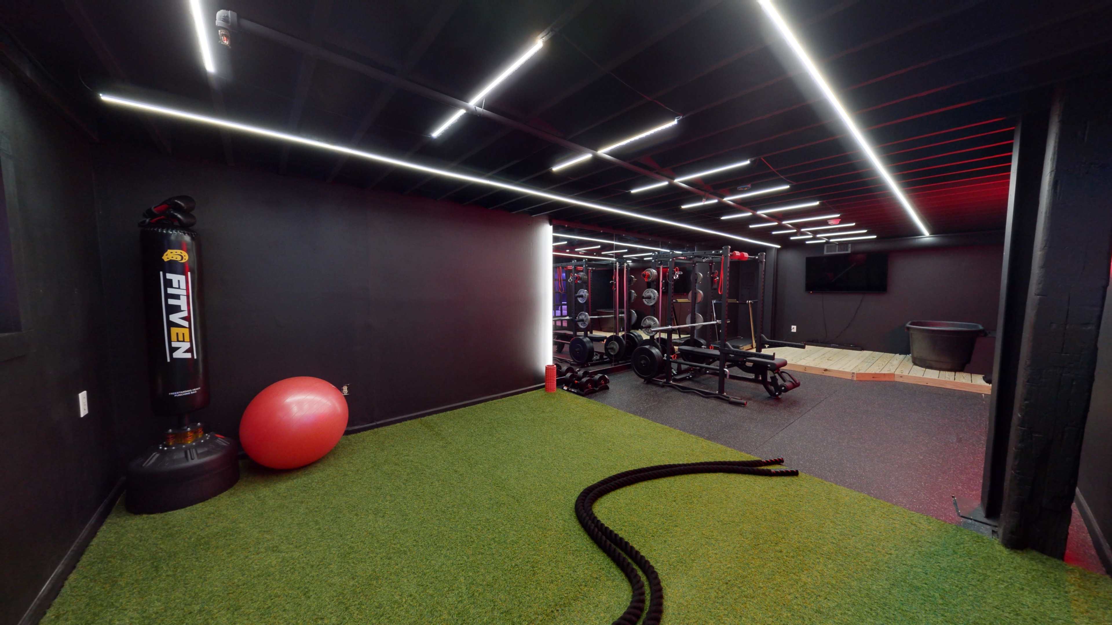 A modern workout space with synthetic grass flooring, exercise equipment, and overhead LED lighting.