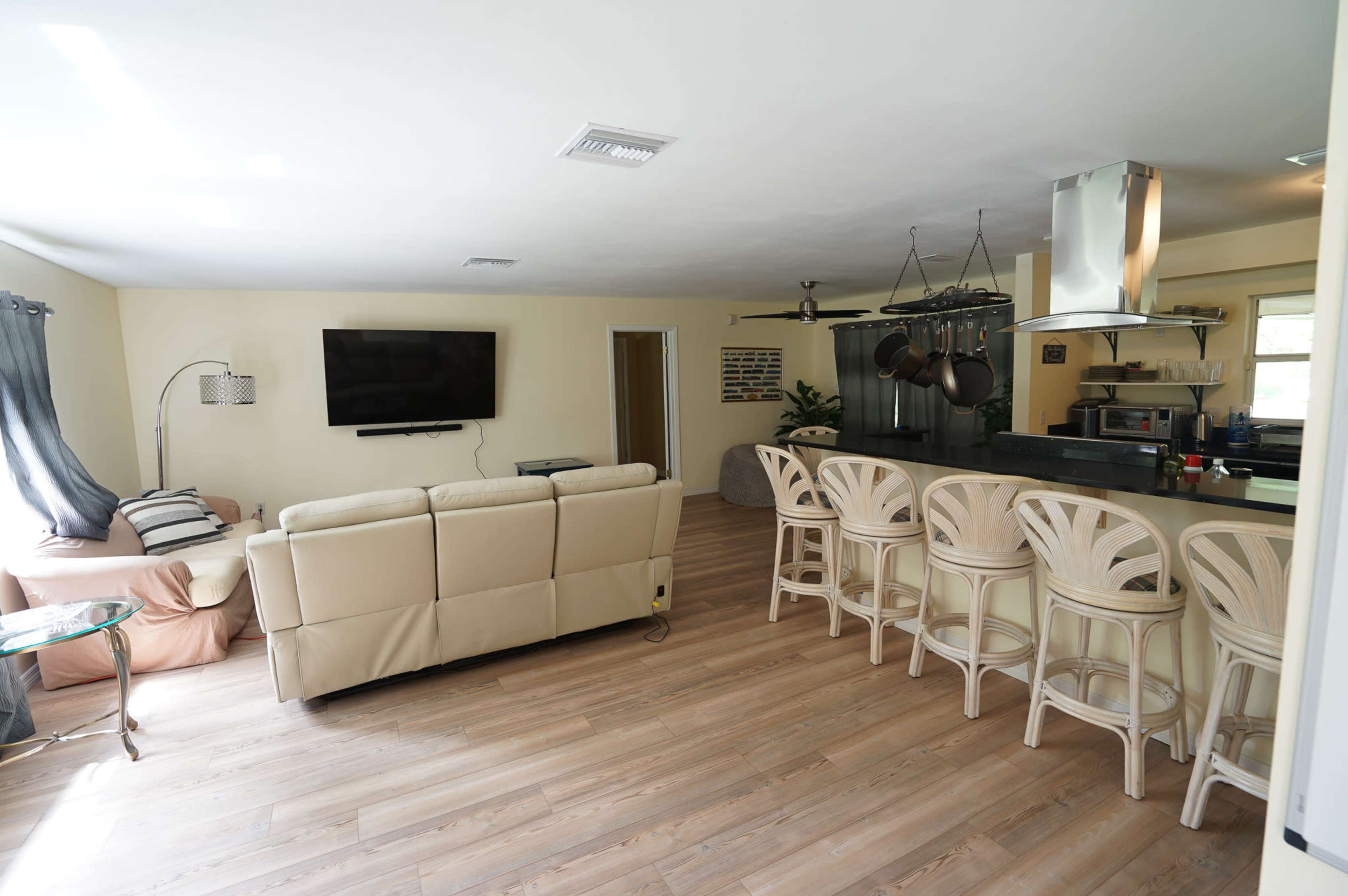 A living room and kitchen area with a sectional sofa, a television mounted on the wall, and a kitchen island with bar stools.