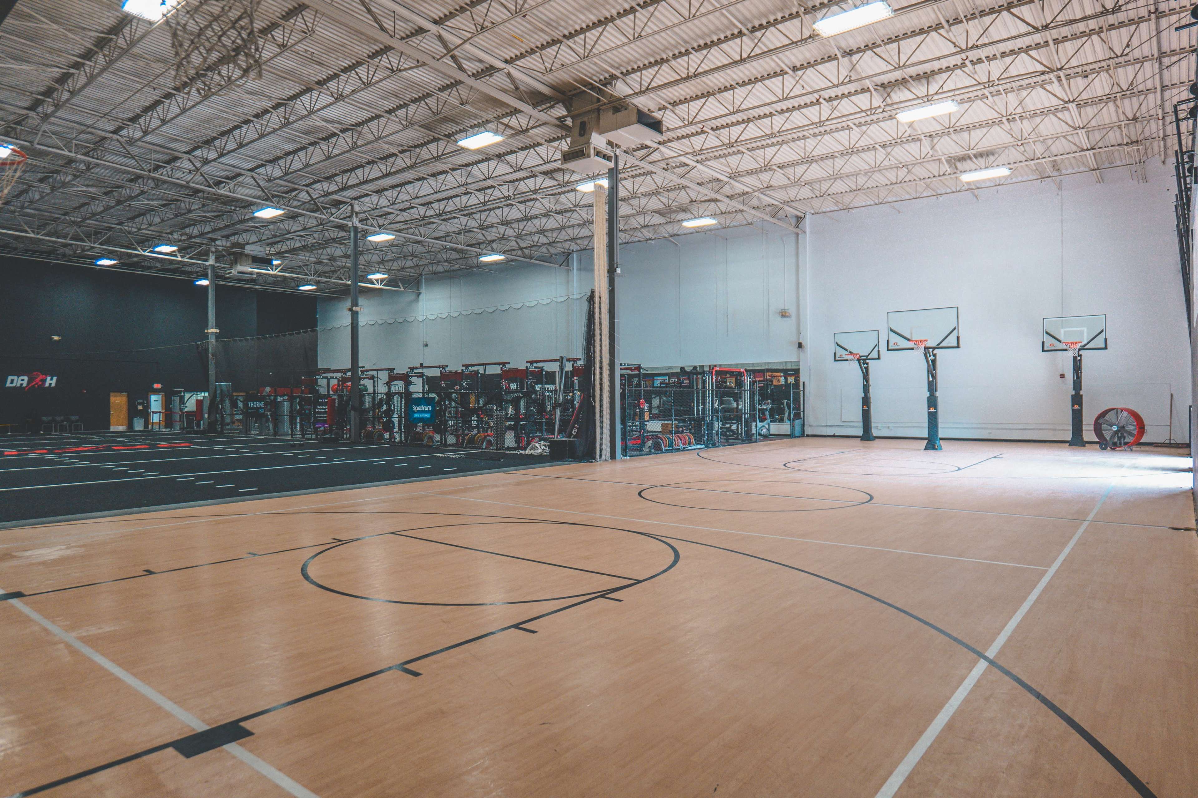 An indoor basketball court with multiple hoops and adjacent workout equipment areas.