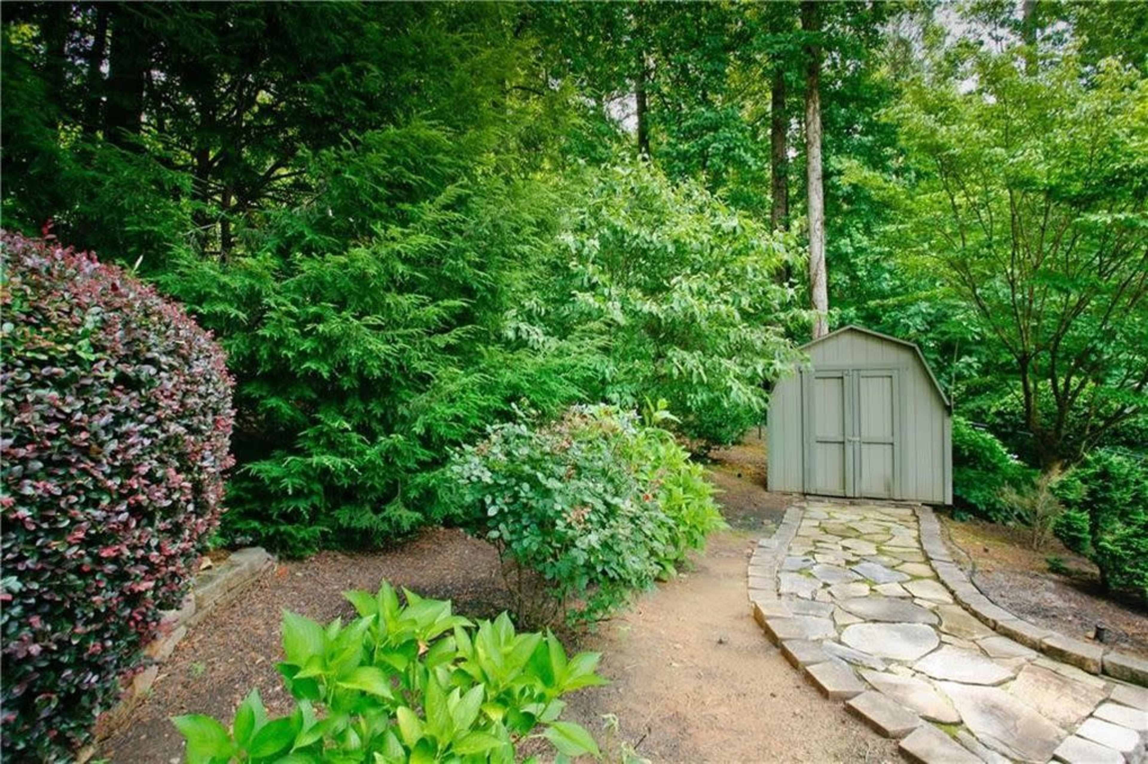 A stone pathway leads to a small shed surrounded by dense greenery and shrubs.
