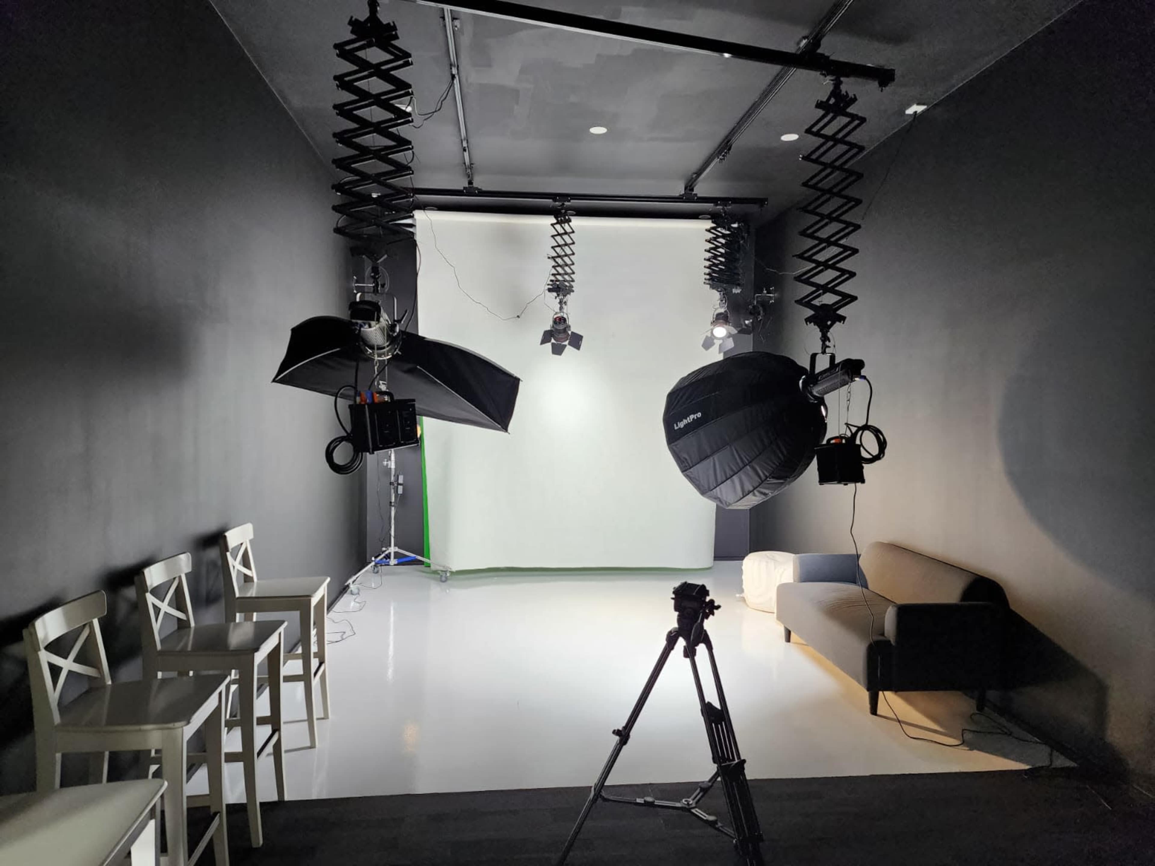 A photography studio is set up with a seamless backdrop, lighting equipment, and a tripod, alongside chairs and a sofa.