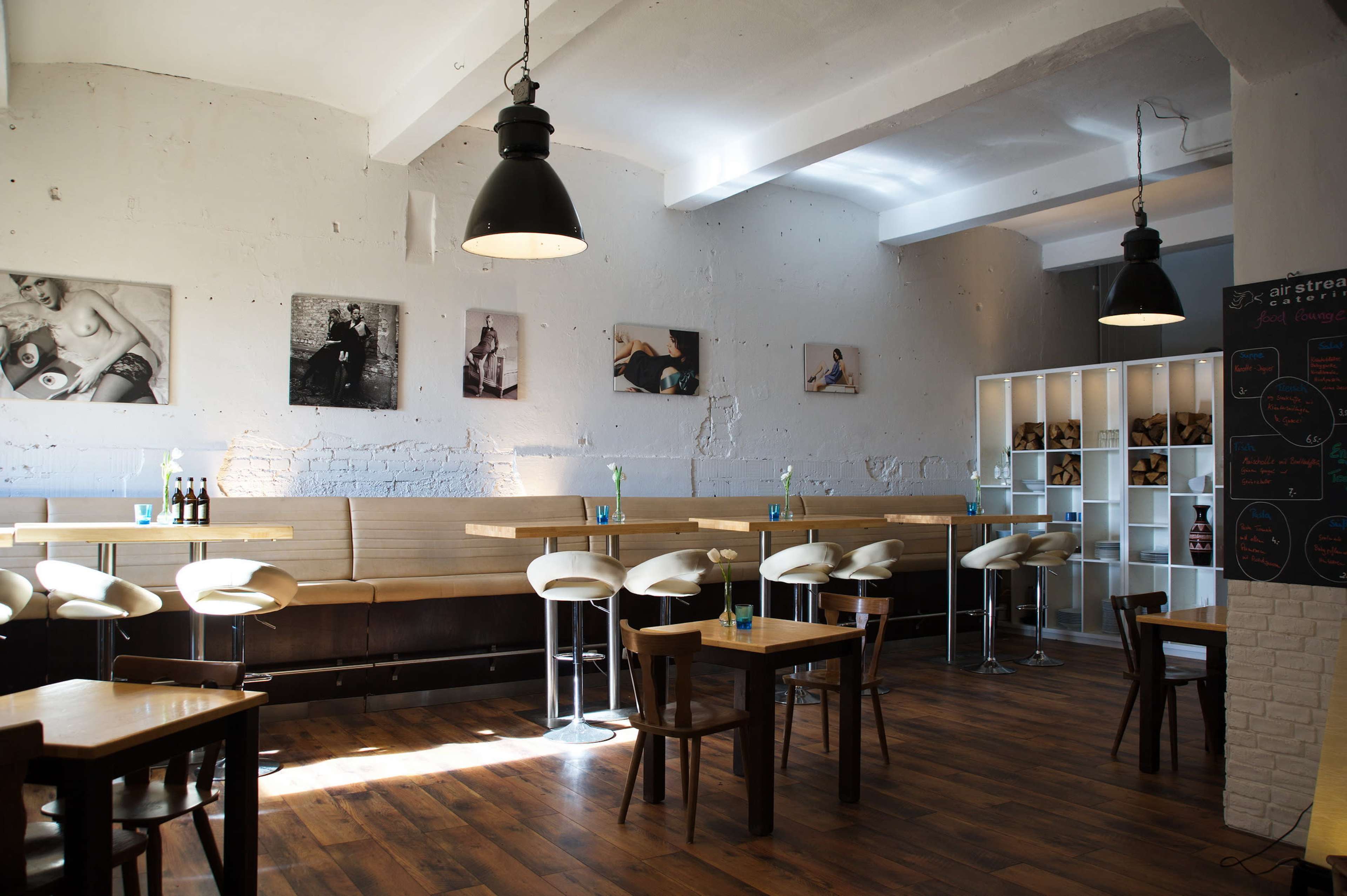 A modern café with wooden floors, high bar stools, and photographs on the walls, illuminated by pendant lights.