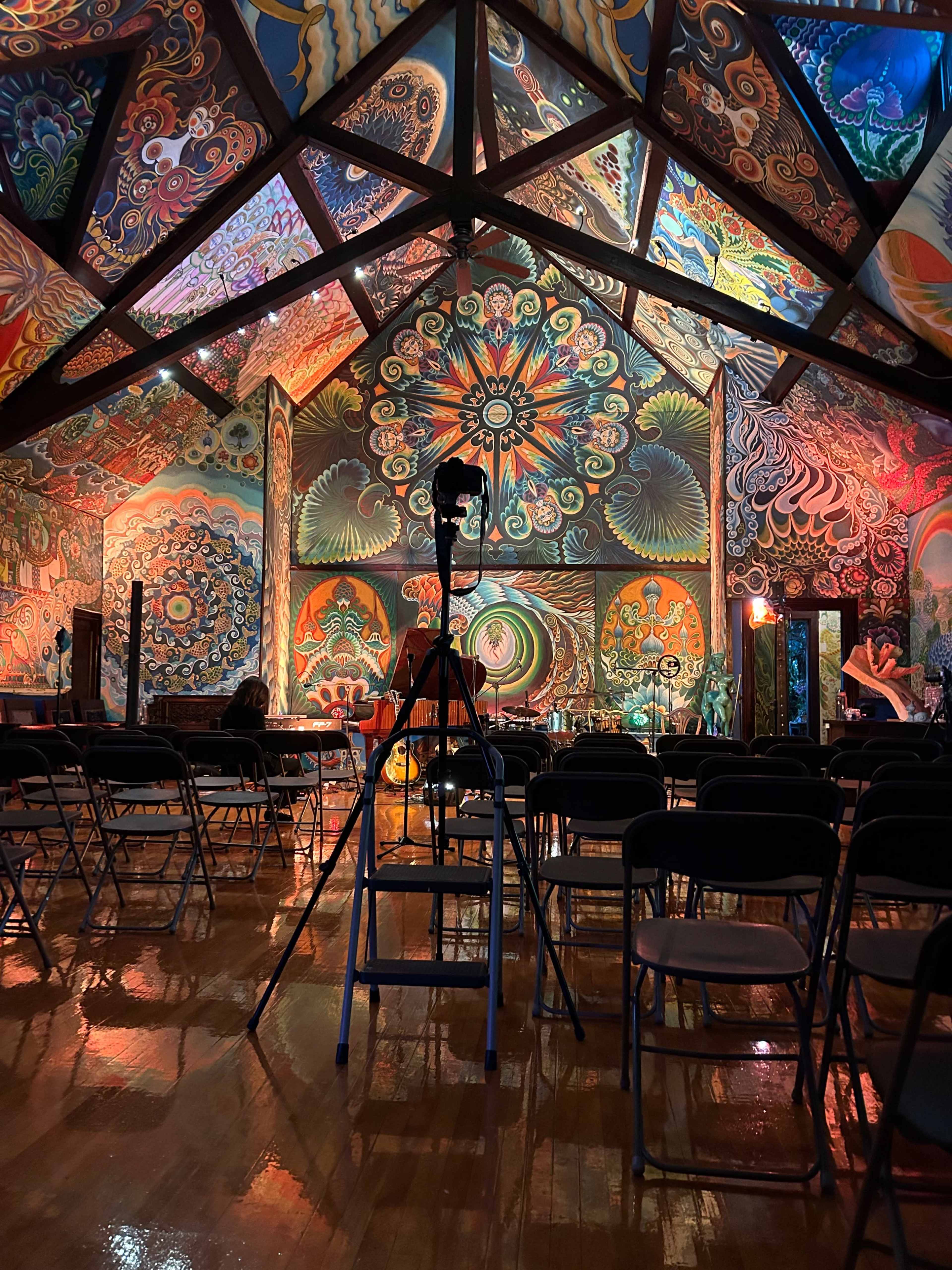 A vibrant mural-covered room with a tripod positioned in front of empty folding chairs.