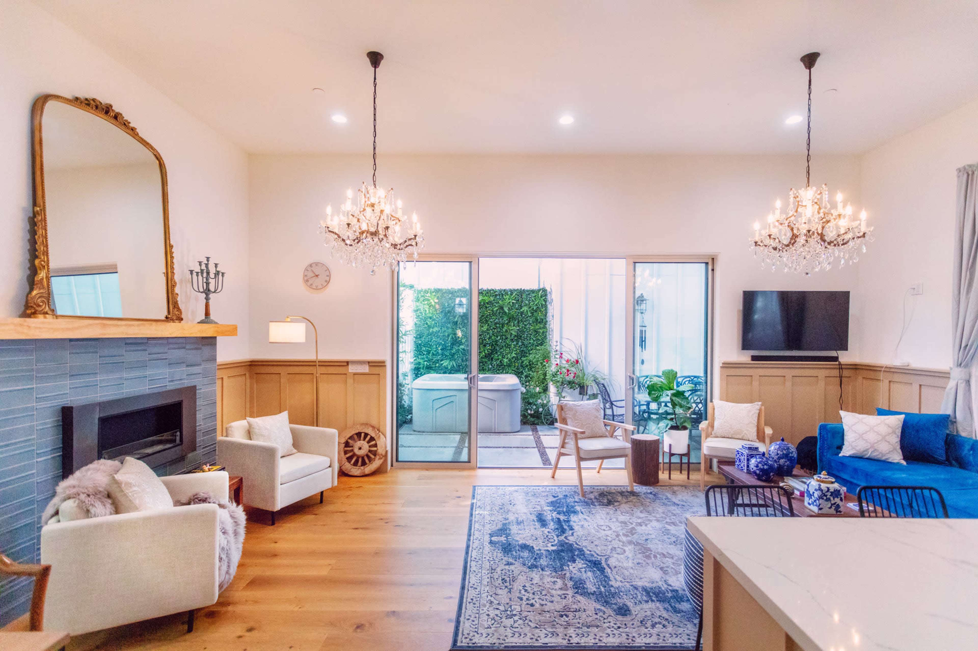 A bright living room with a fireplace, a large mirror, two chandeliers, a blue sofa, and a view of a patio through sliding glass doors.