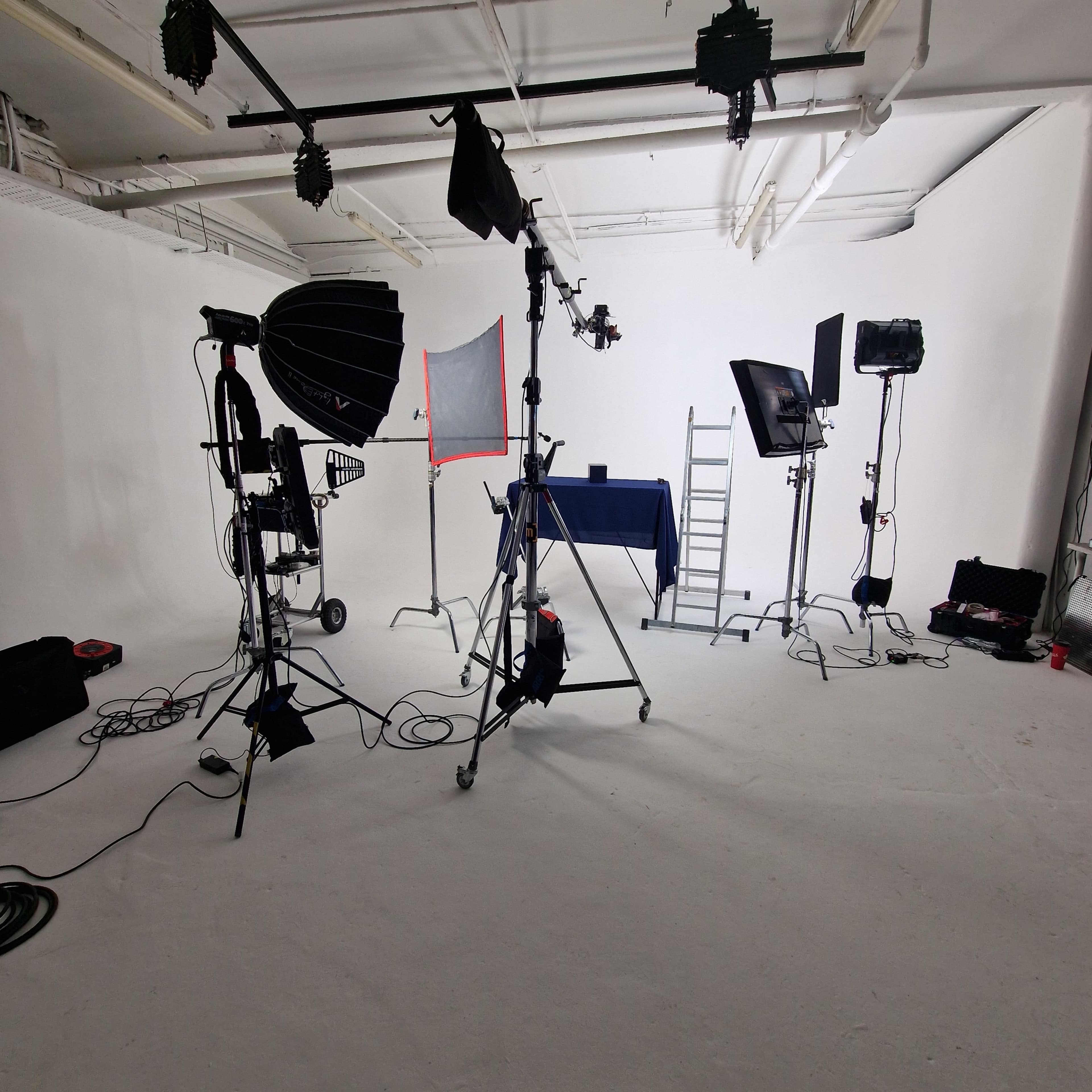 A photography studio setup with various lighting equipment, stands, and a table in front of a white backdrop.