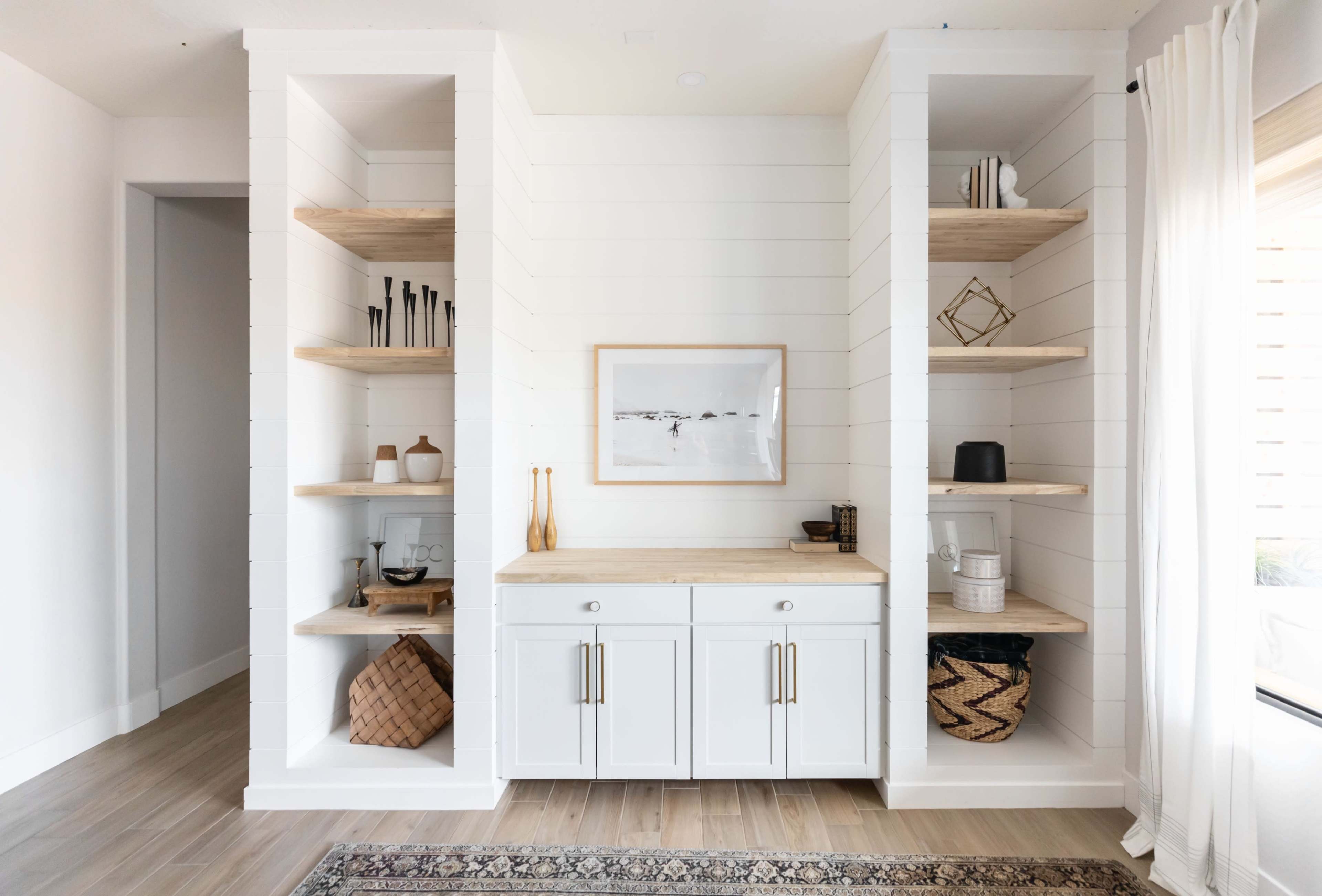 A minimalist shelving unit with white wooden frames and natural wood shelves, flanking a central cabinet, all positioned against a light-colored wall.