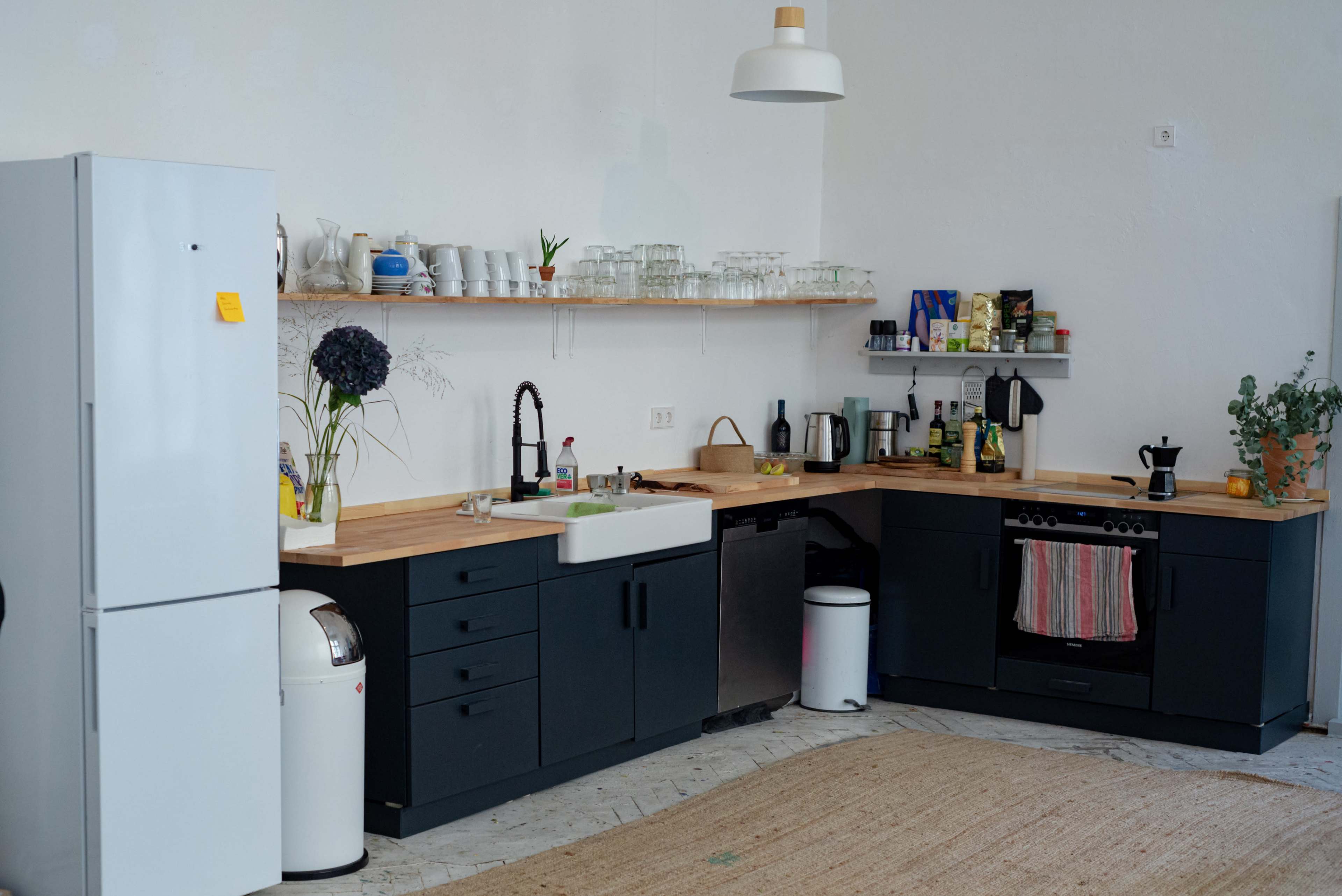 The image shows a modern kitchen featuring a blend of black cabinets, a wooden countertop, a white farmhouse sink, and various kitchen appliances.