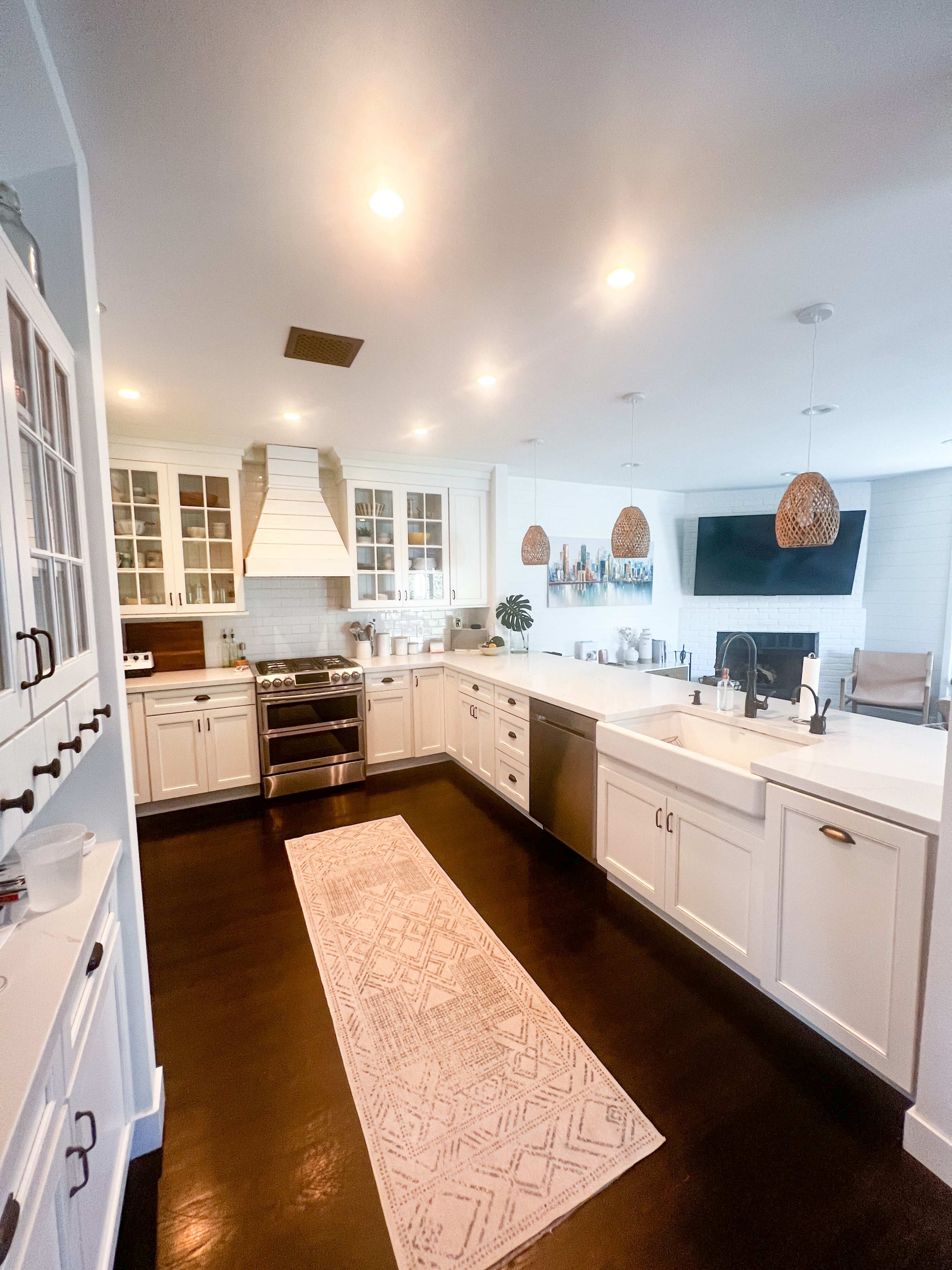 A modern kitchen with white cabinets, stainless steel appliances, a large island, and a patterned rug running along the floor.