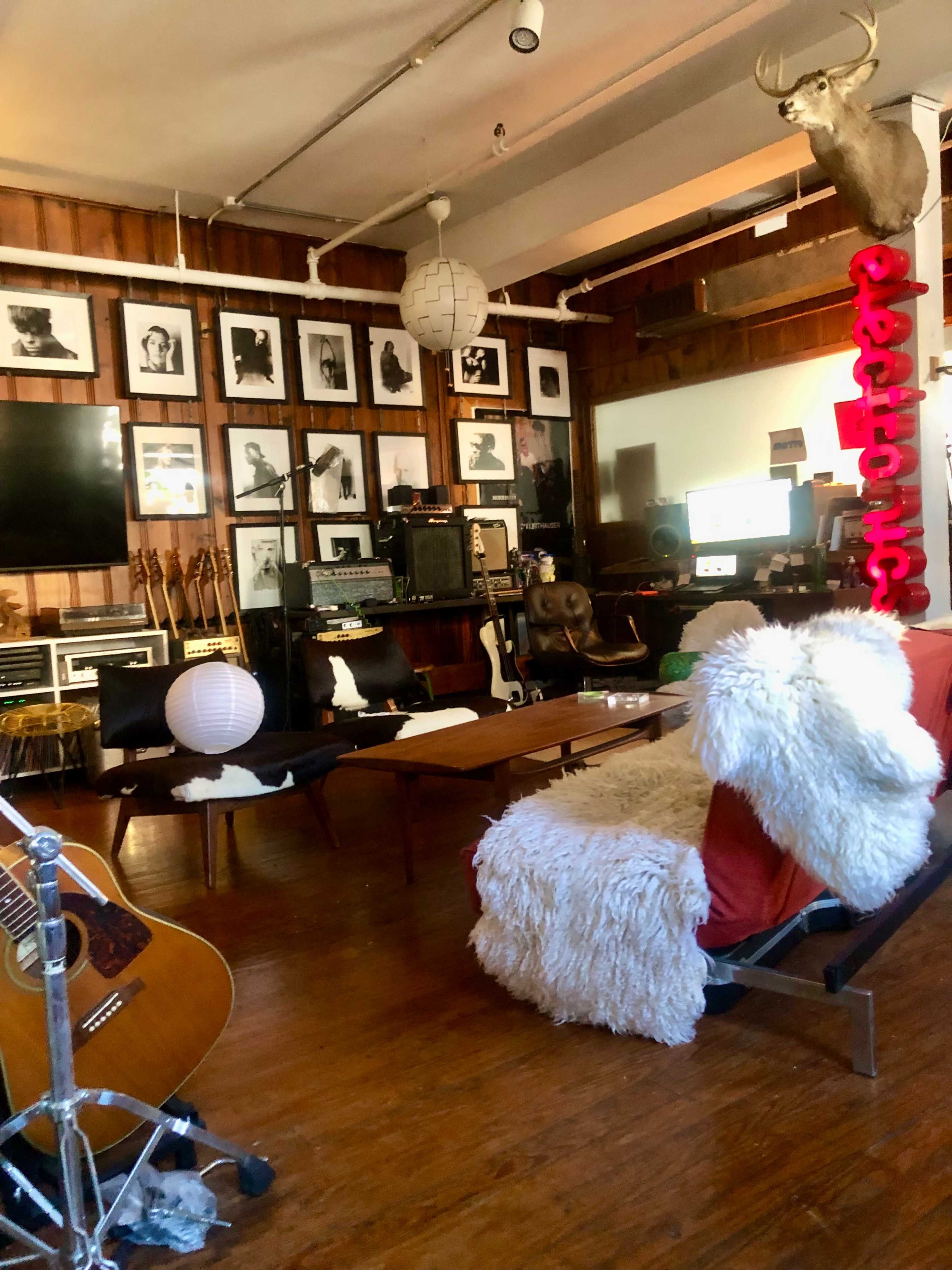 The room features a cozy seating area with a white fur throw, musical instruments, framed photographs on the wooden walls, and a vintage television setup.