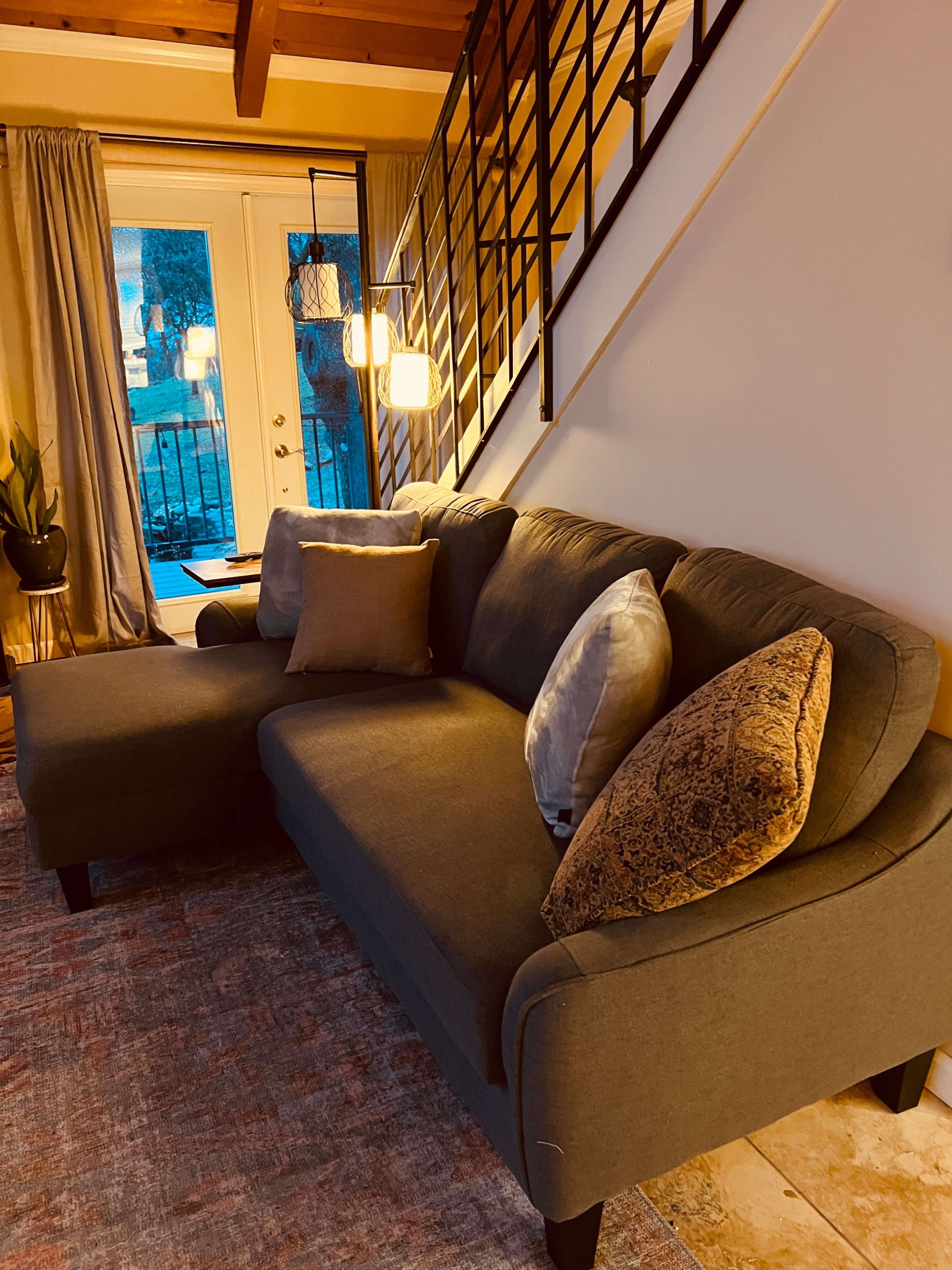 A gray sectional sofa with decorative pillows sits in a well-lit living room near a staircase and a glass door.