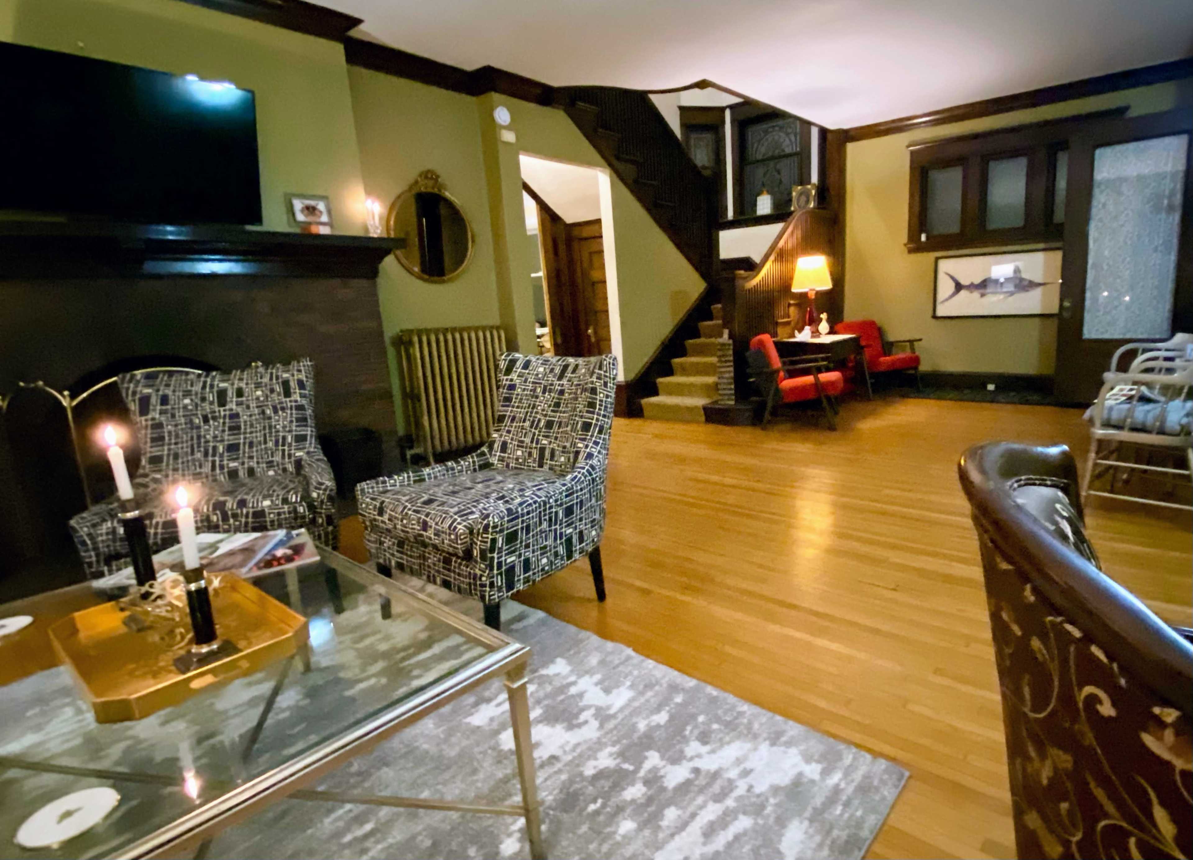The room features a seating area with patterned chairs, a glass coffee table, and a staircase leading to an upper level.