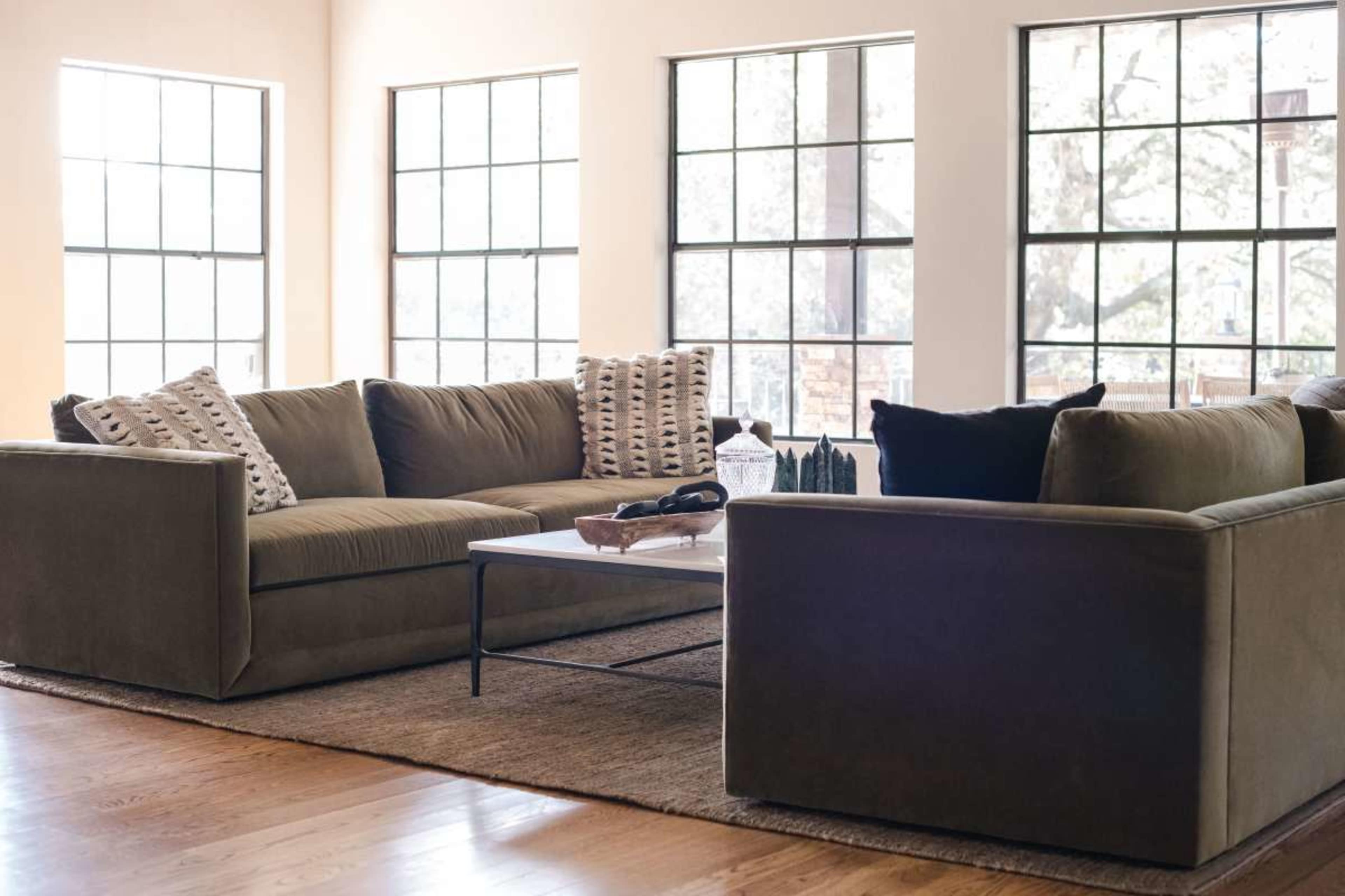 The image shows a modern living room with a sectional sofa, a coffee table, and large windows that allow natural light to fill the space.