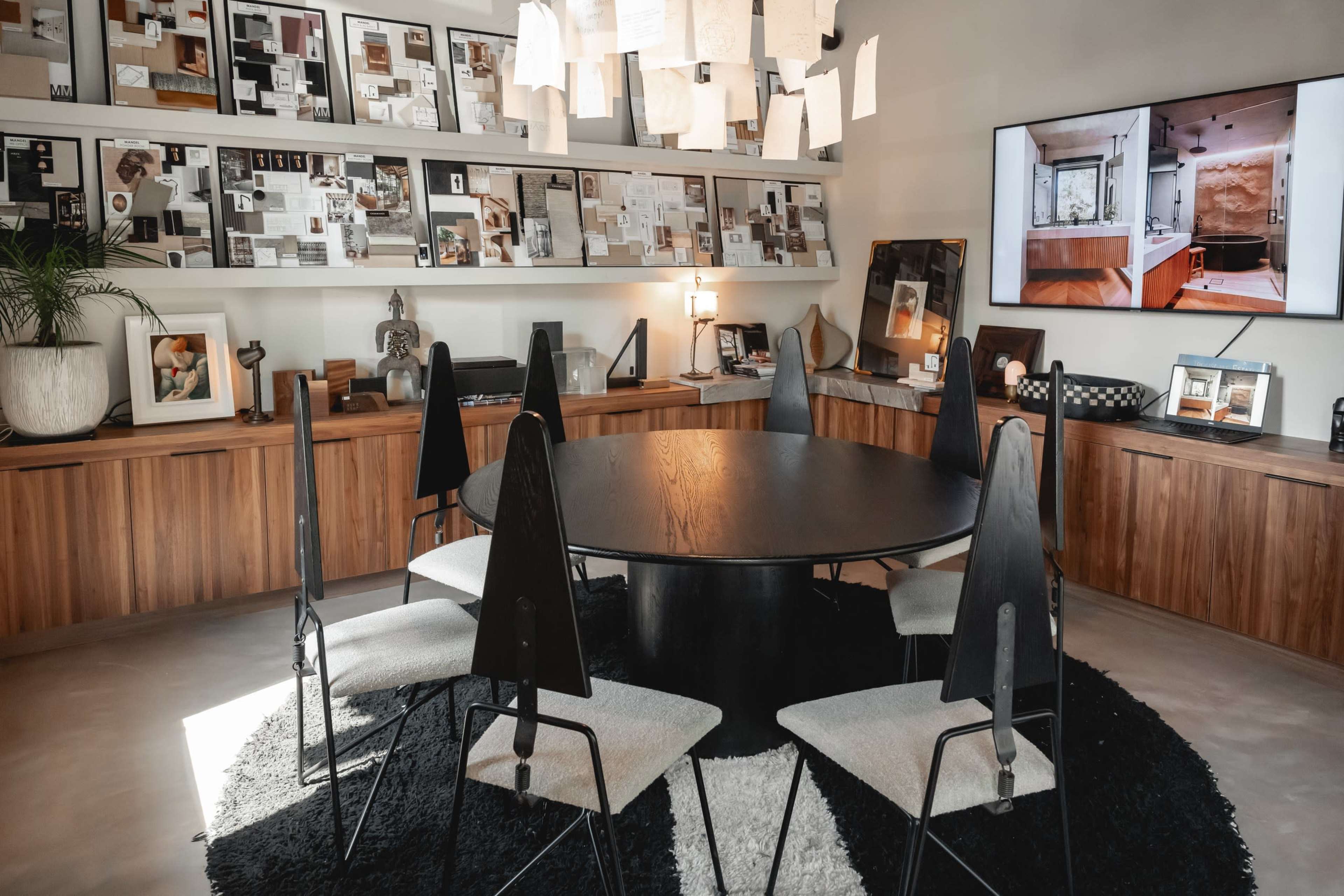 A modern conference room with a round black table surrounded by six black chairs, accentuated by a large display screen and various framed images and notes on the walls.