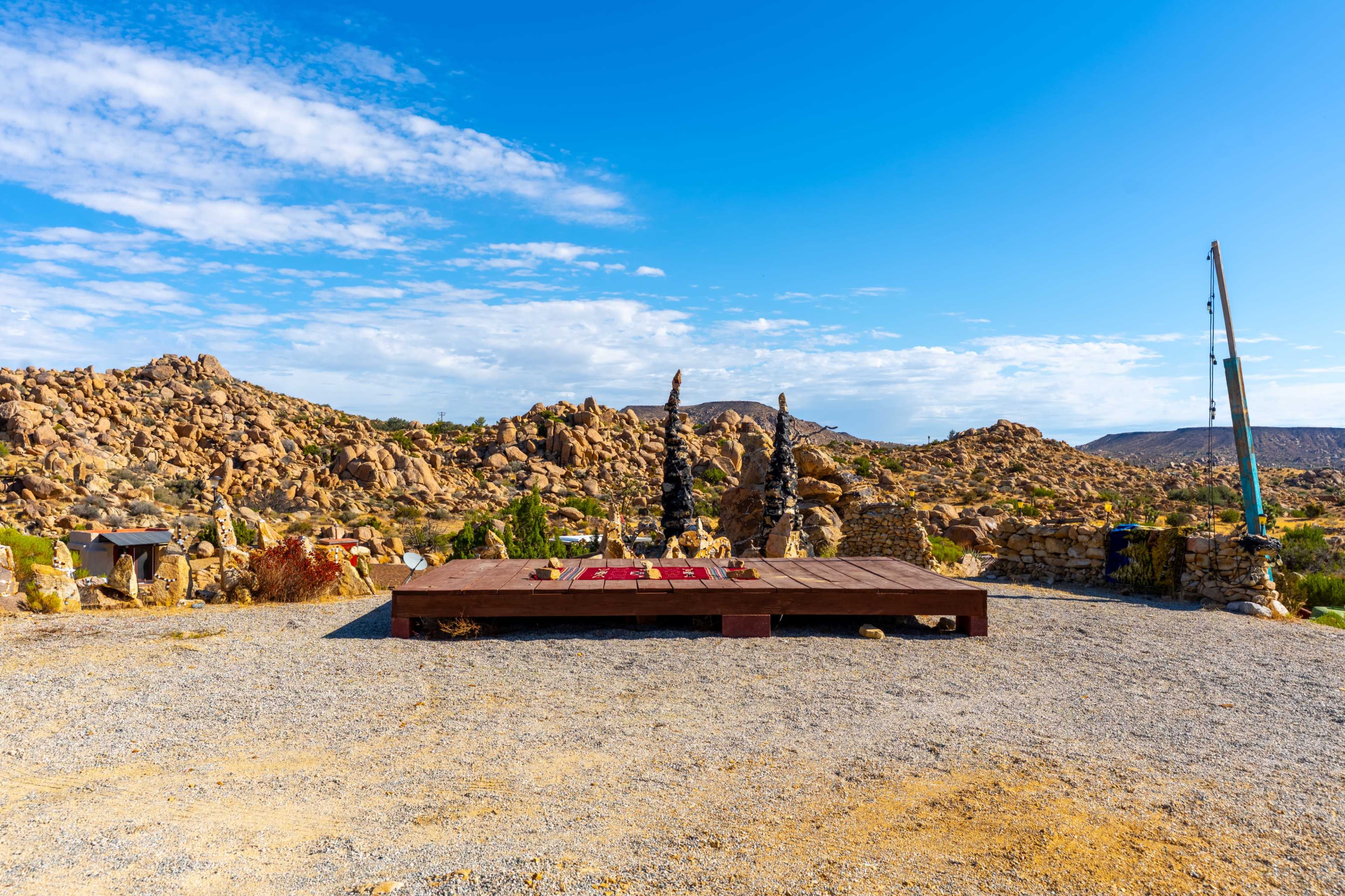 A wooden platform is centered in a rocky desert landscape under a blue sky with scattered clouds.