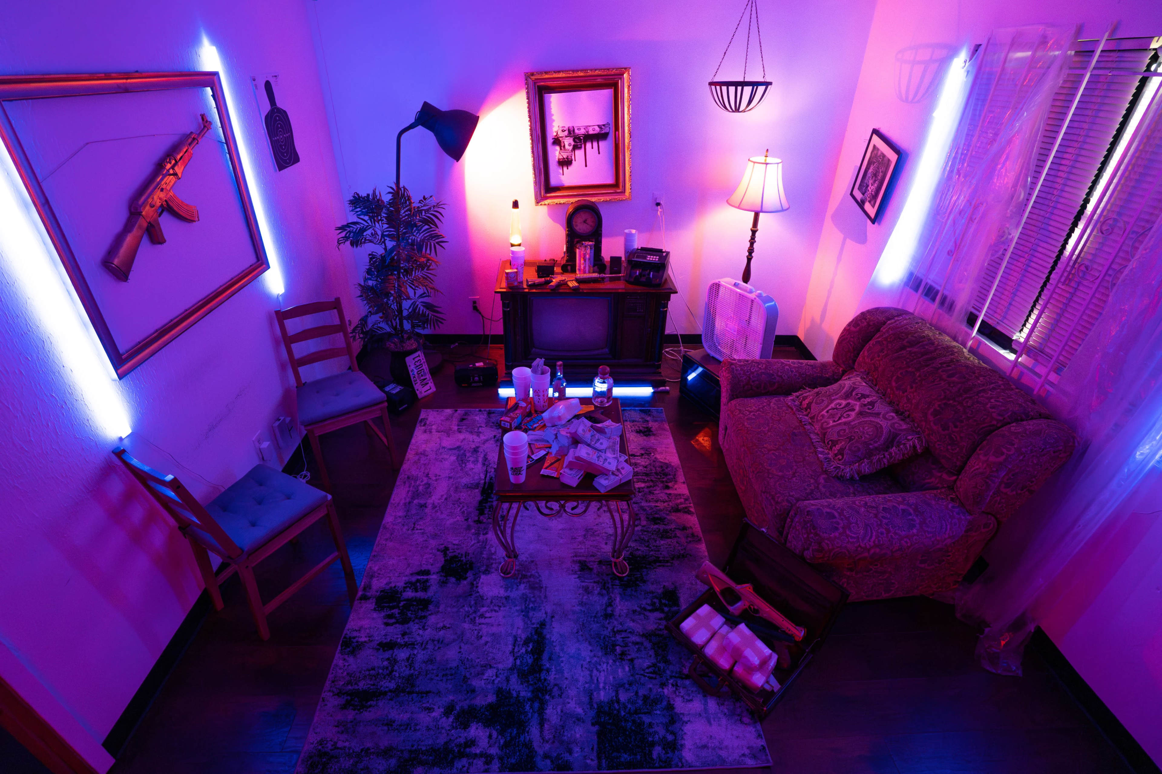 The image depicts a brightly lit living room featuring a couch, a coffee table with scattered items, a television, and various decorations, all illuminated by purple and blue lighting.