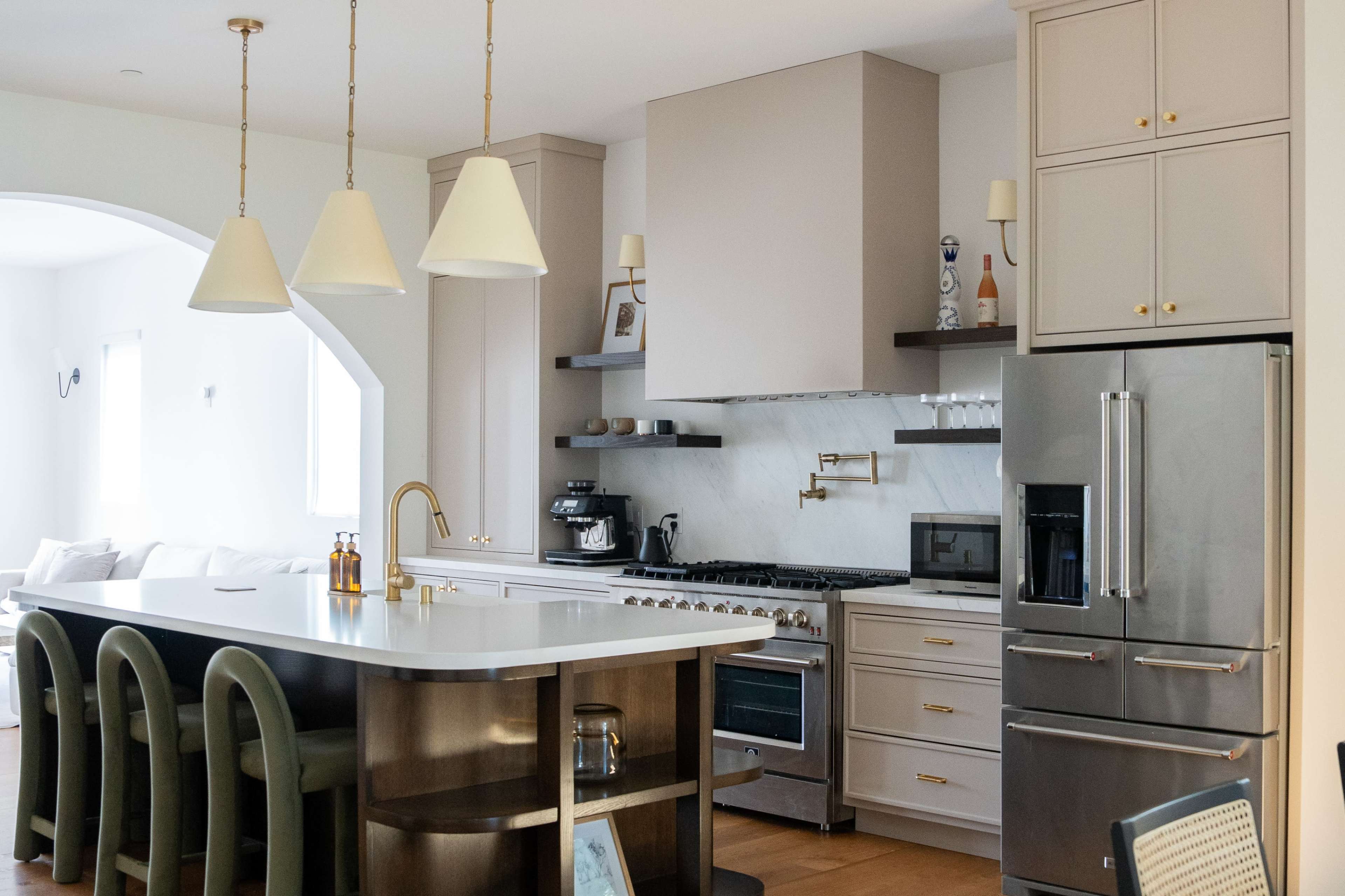 A modern kitchen featuring a large island with a white countertop, stainless steel appliances, and wooden accents.