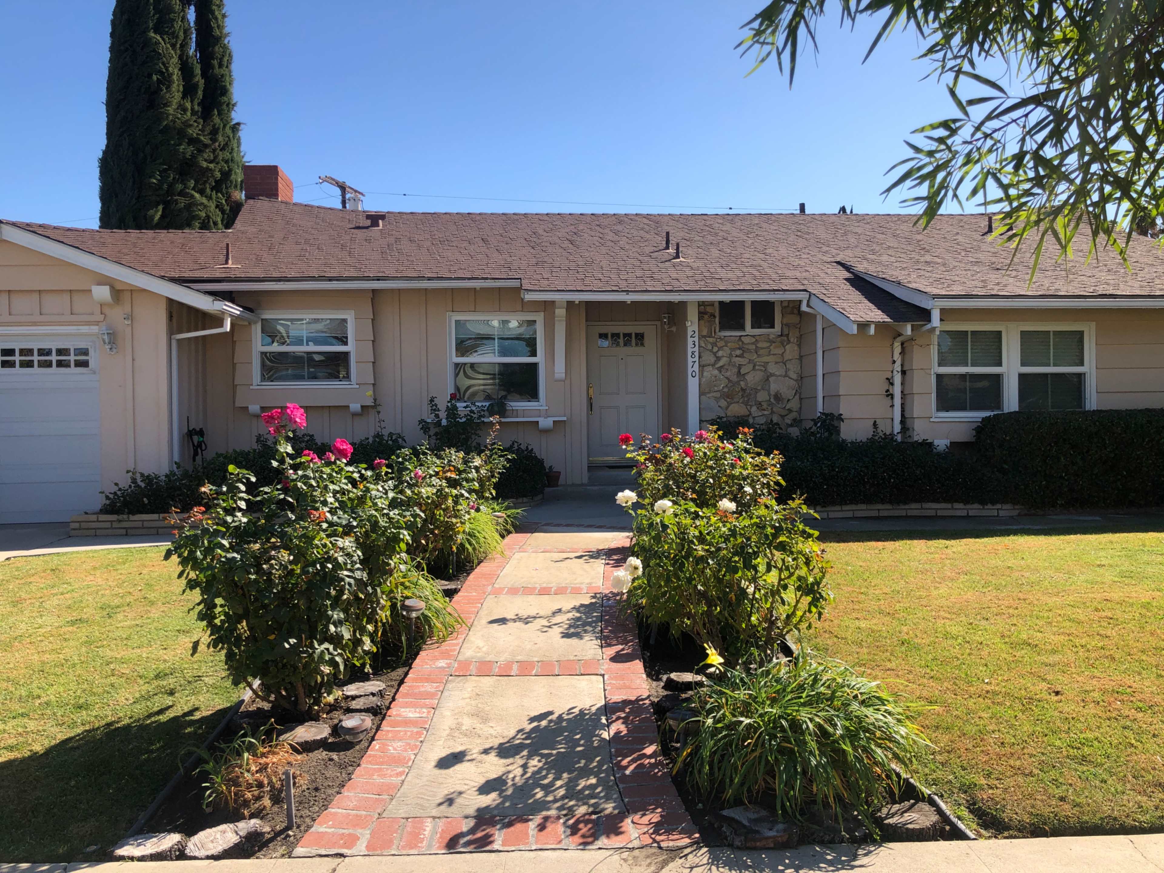 A single-story house with a front walkway bordered by flower beds and a neatly maintained lawn.