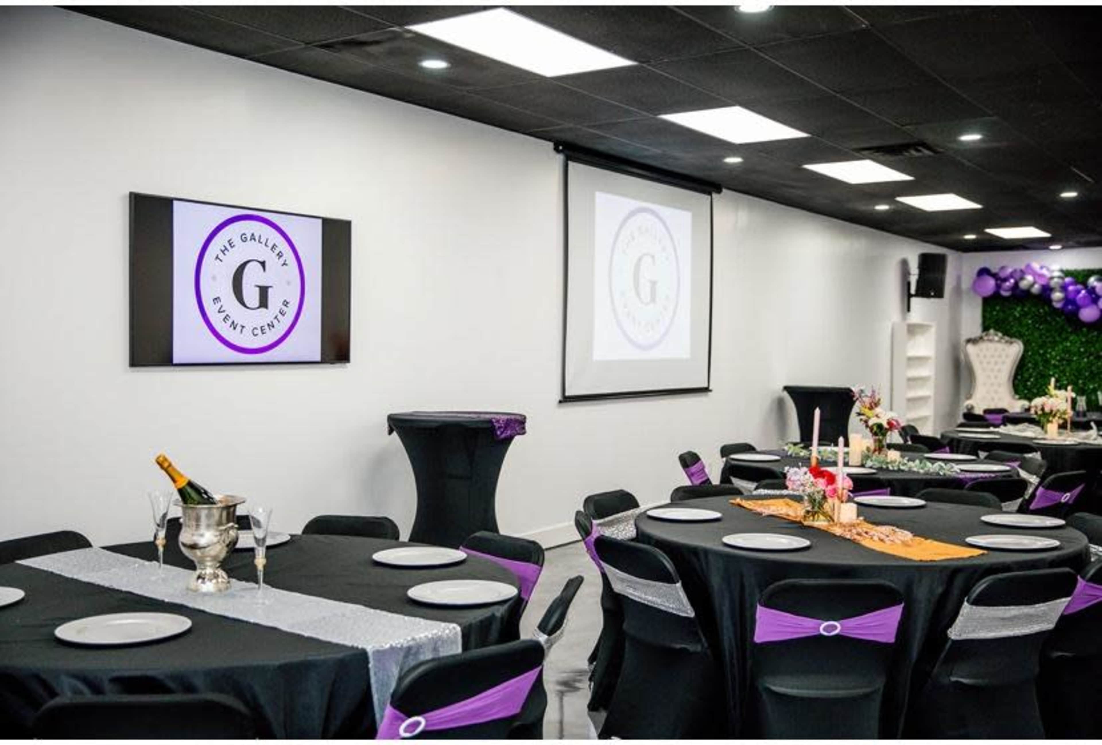 An elegantly set event center featuring black tables with purple accents, a screen displaying the event center's logo, and decorative elements on the tables.