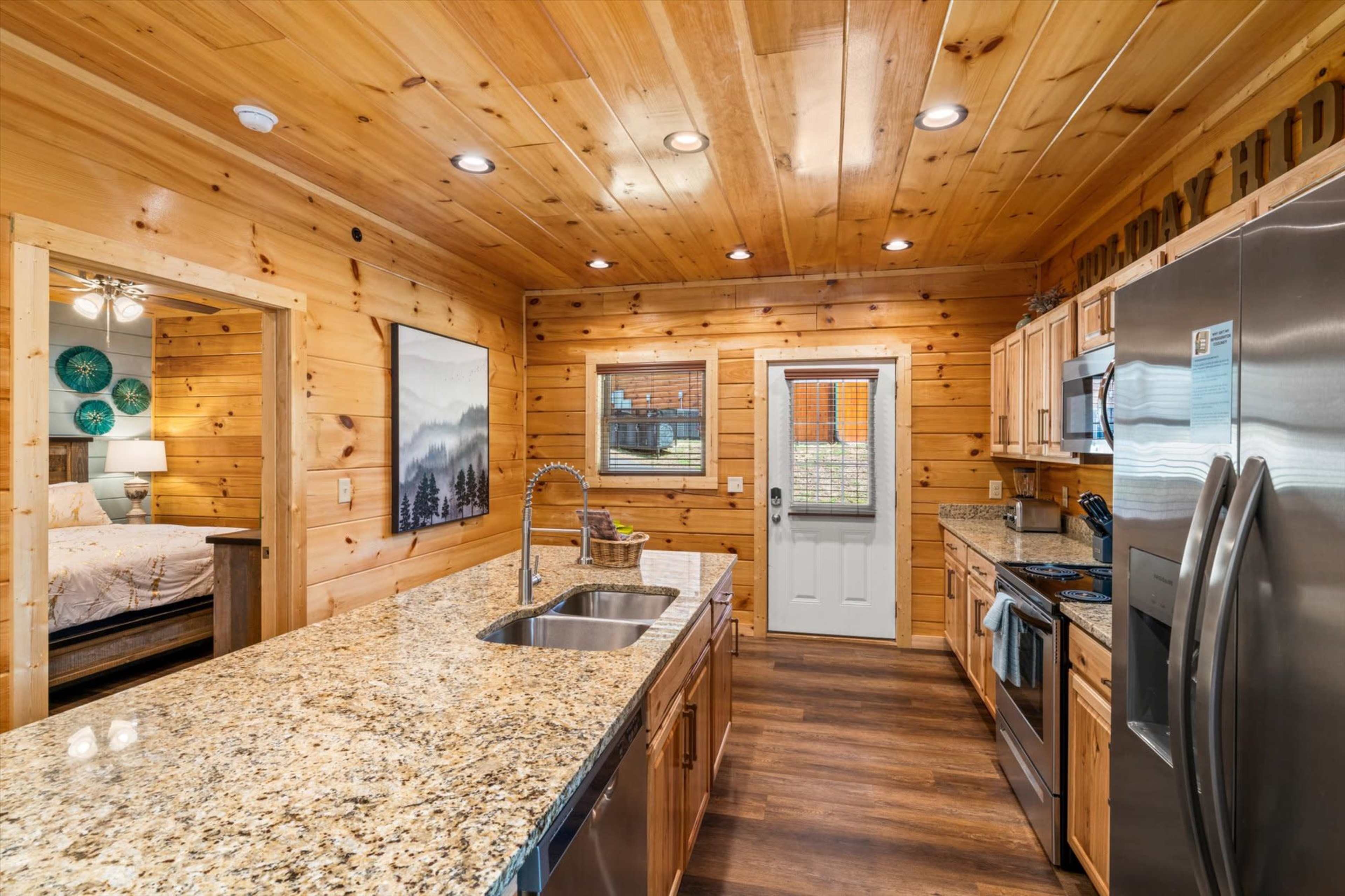 A cozy kitchen with wooden walls, granite countertops, stainless steel appliances, and a view of a door leading outside.