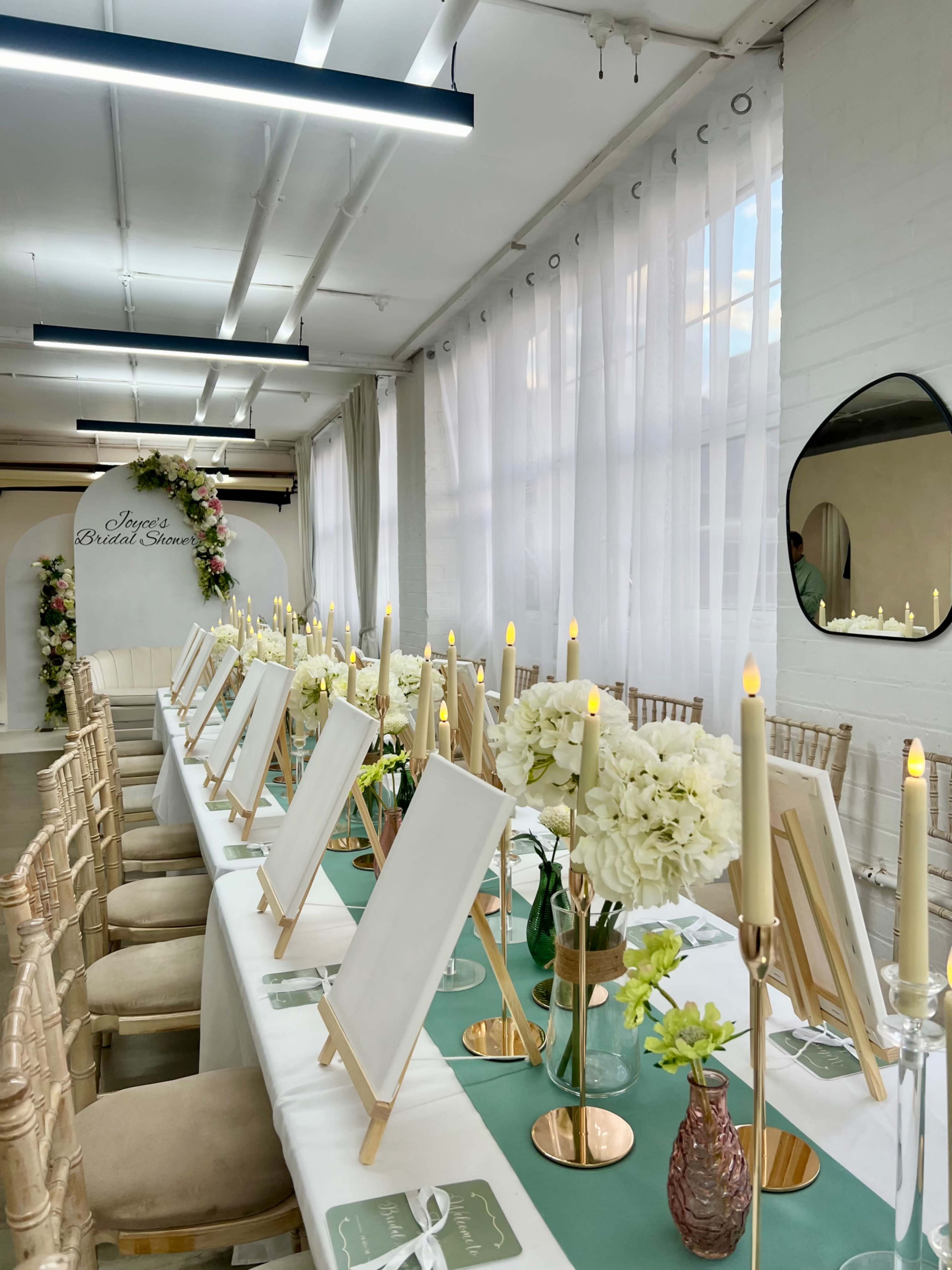 A long banquet table is set with easels, flowers, and candles in a bright, modern room.