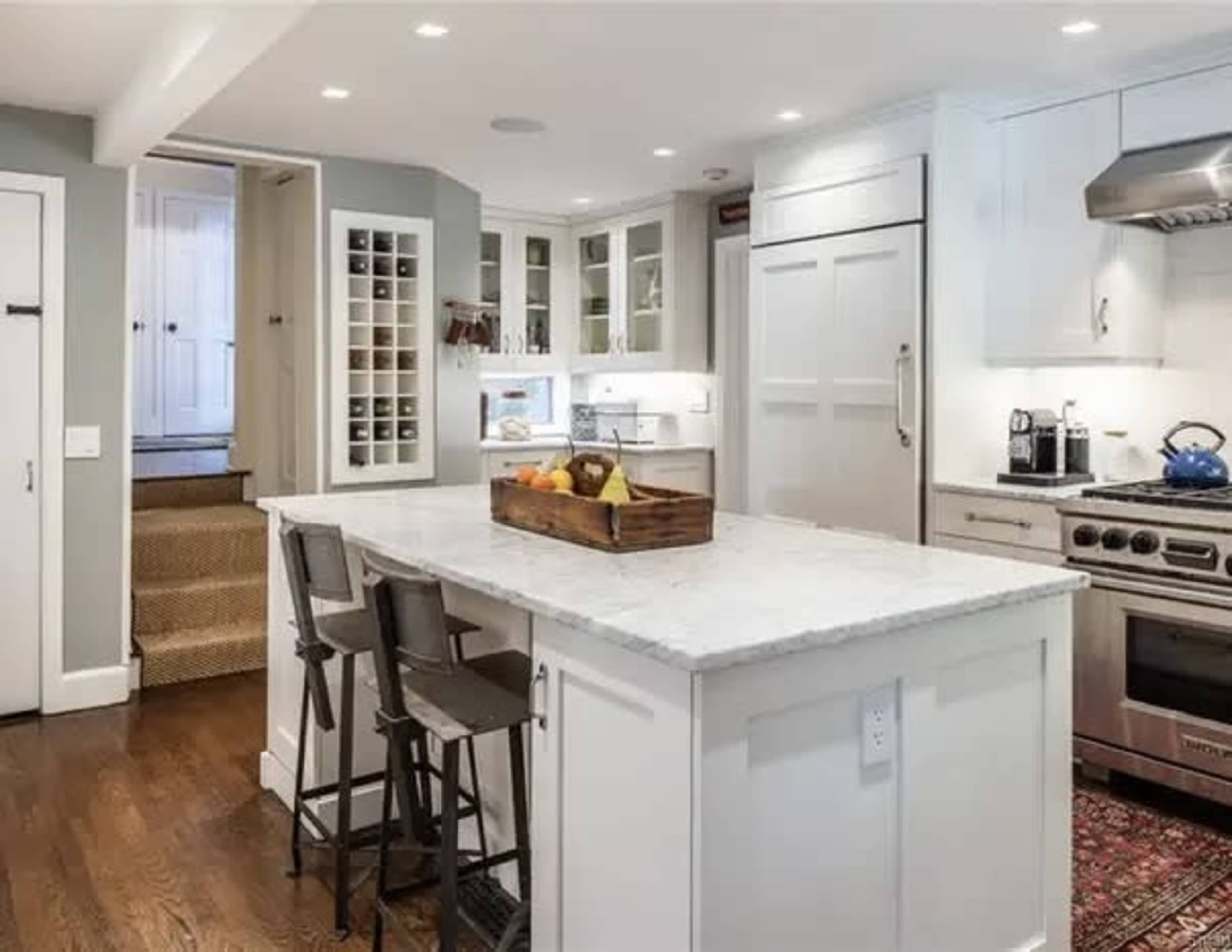 A modern kitchen featuring a central island with a marble countertop, stainless steel appliances, and a staircase leading to an upper level.