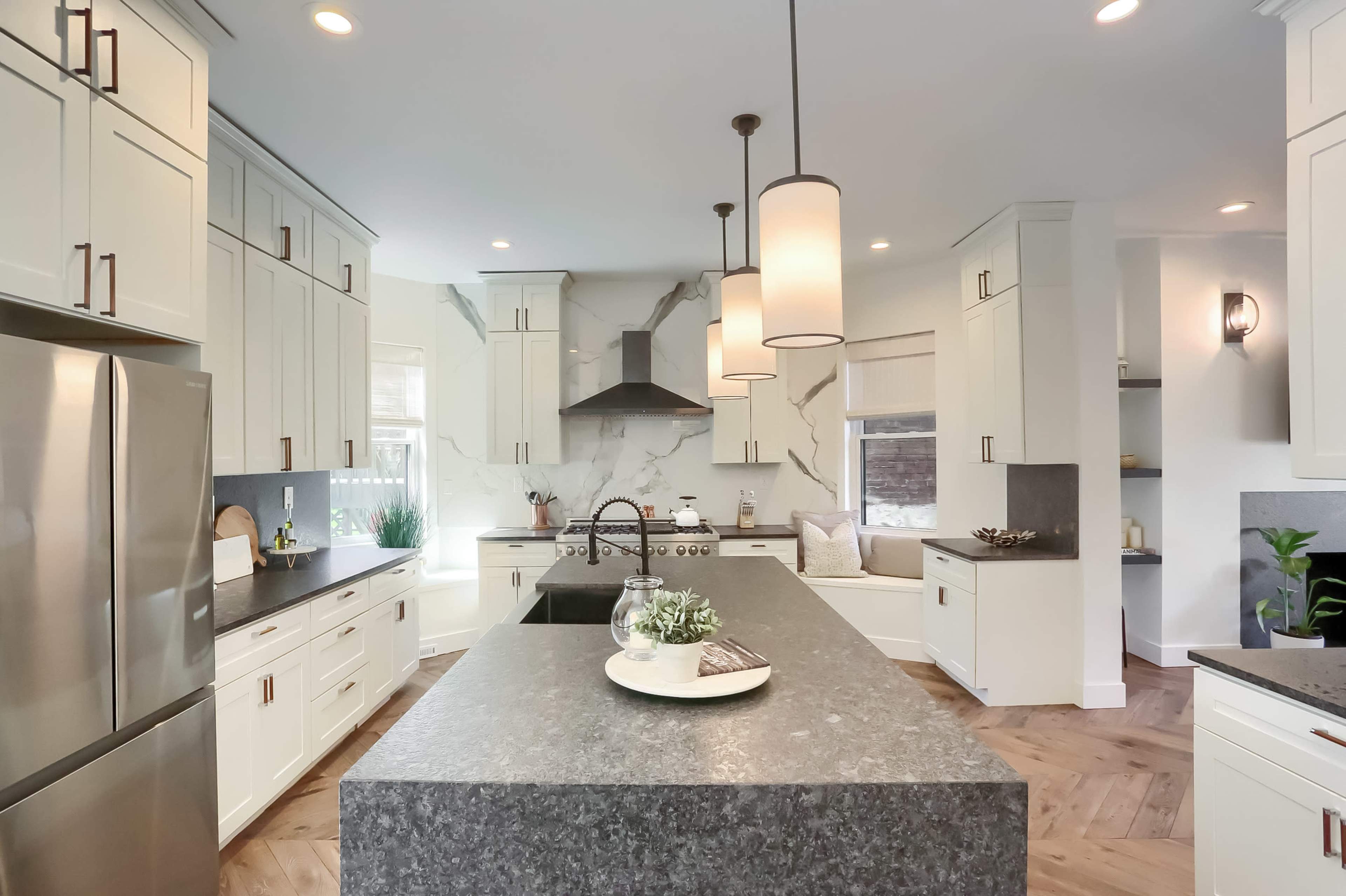 A modern kitchen features white cabinetry, a large central island with a dark countertop, and stainless steel appliances.