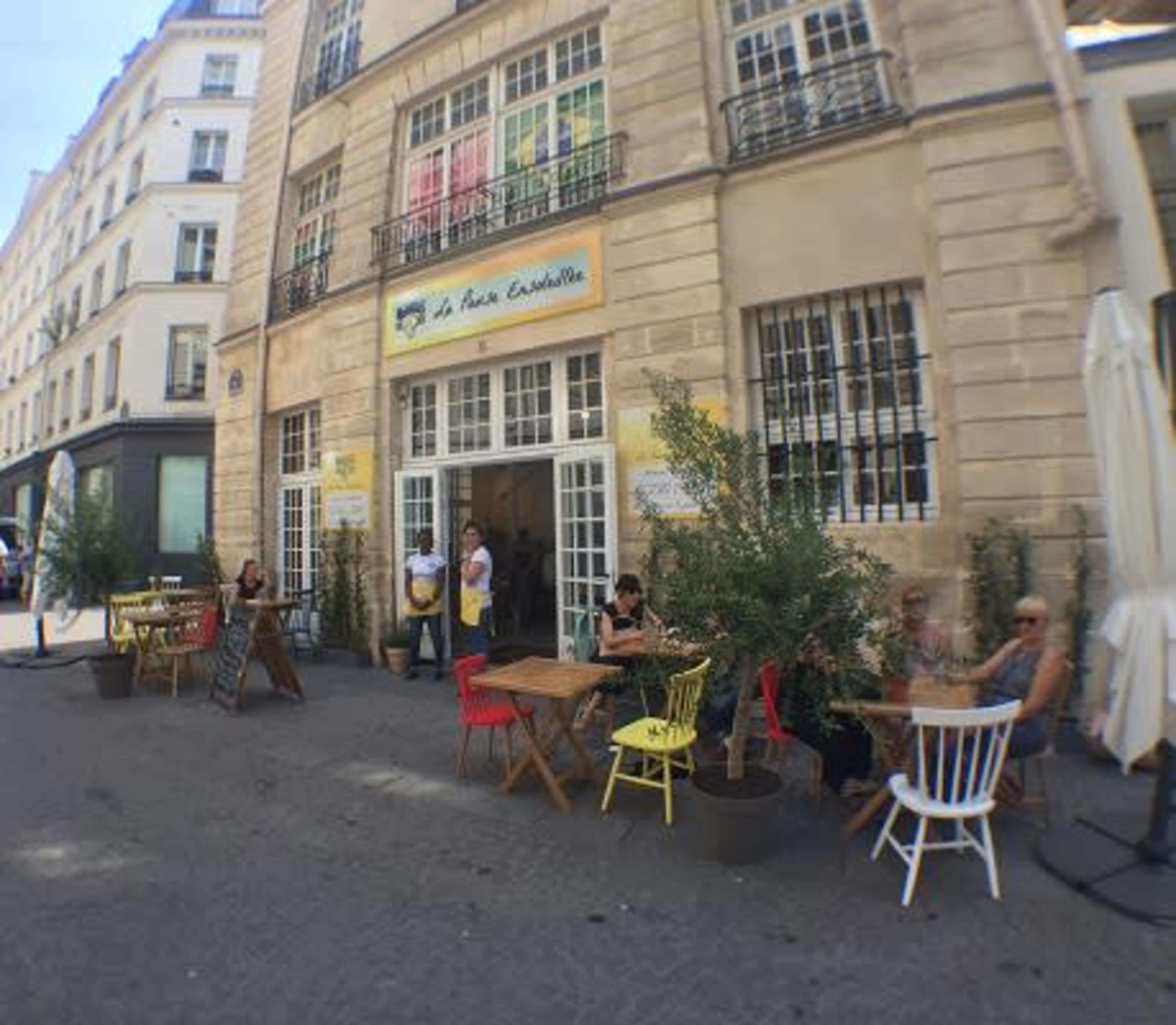 A café with outdoor seating, featuring colorful chairs and people dining on a cobblestone street.