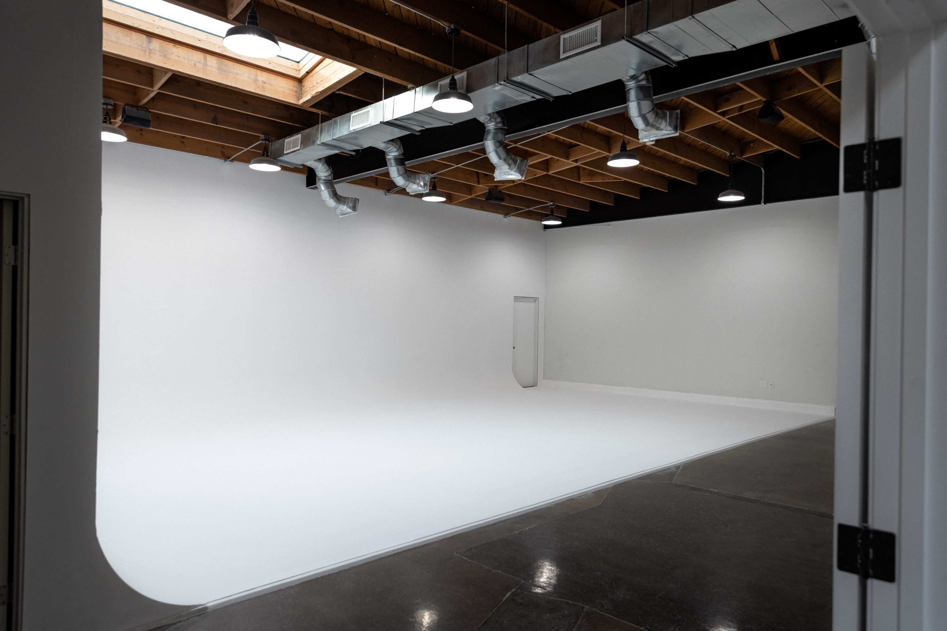 The image shows a spacious, empty studio with white walls and a seamless backdrop, illuminated by overhead lights.
