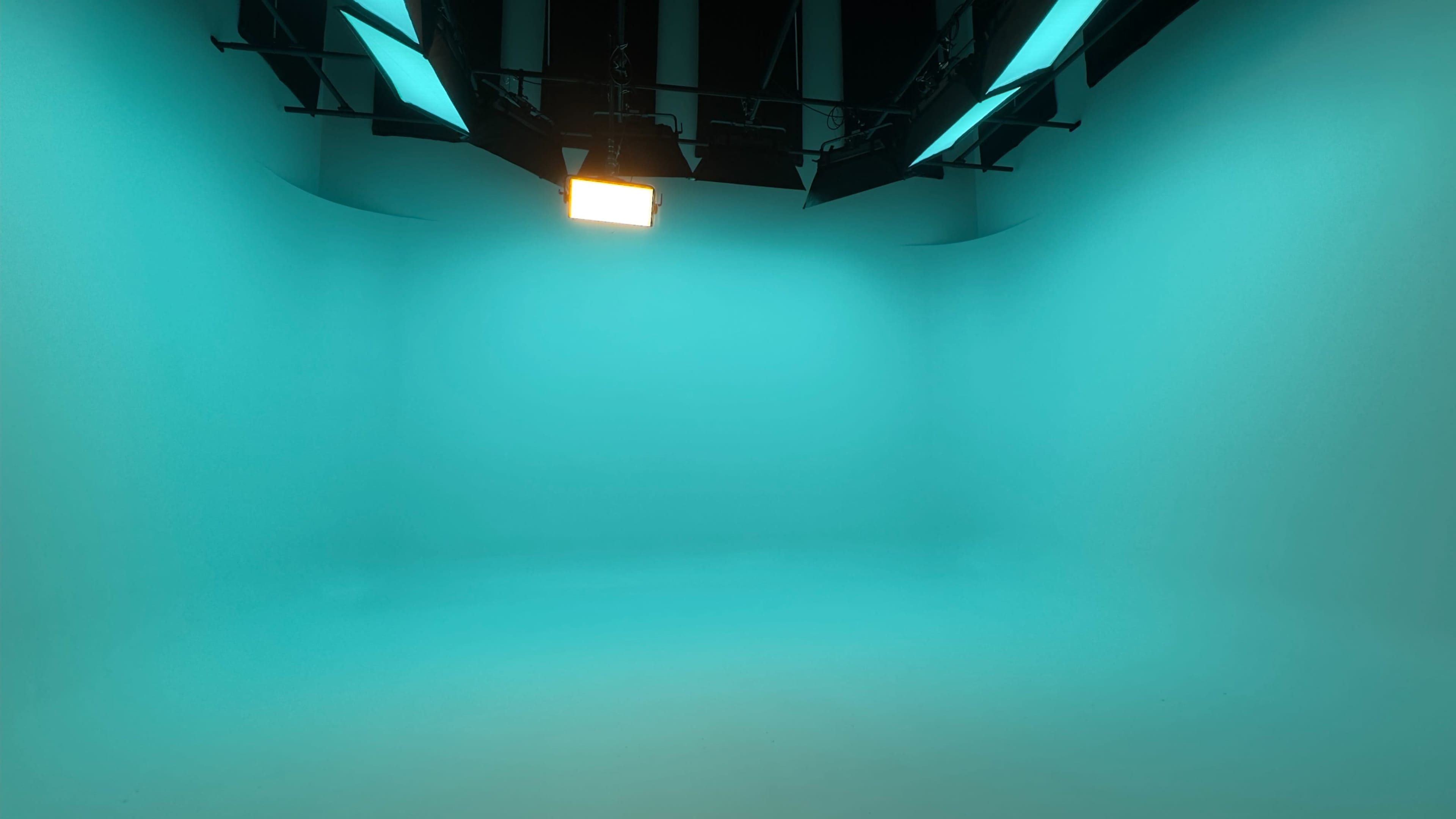 The image shows an empty studio space with a bright teal backdrop and overhead lighting.