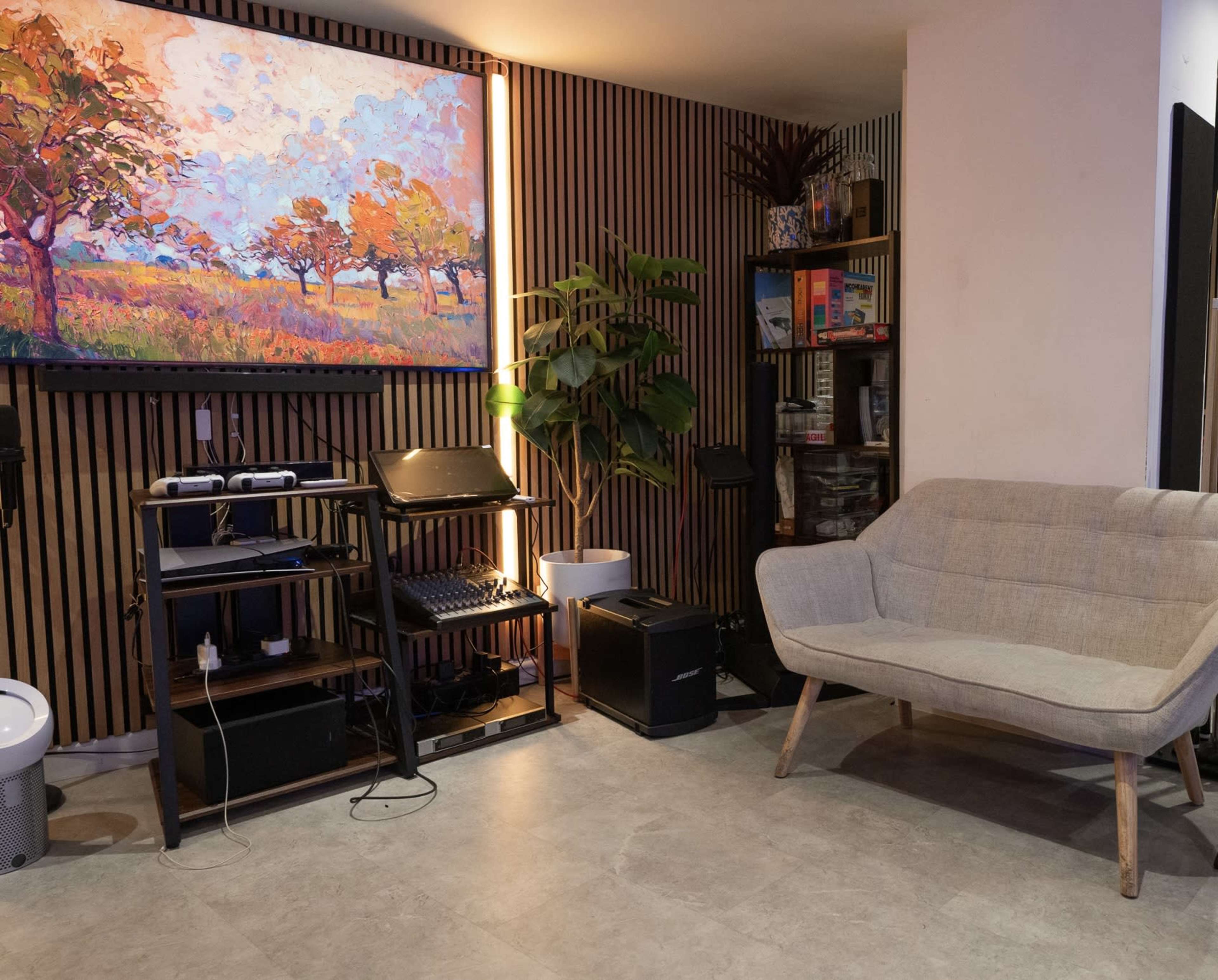 The scene features a cozy, modern living area with a light-colored sofa, a computer station, a potted plant, and a vibrant landscape painting on the wall.