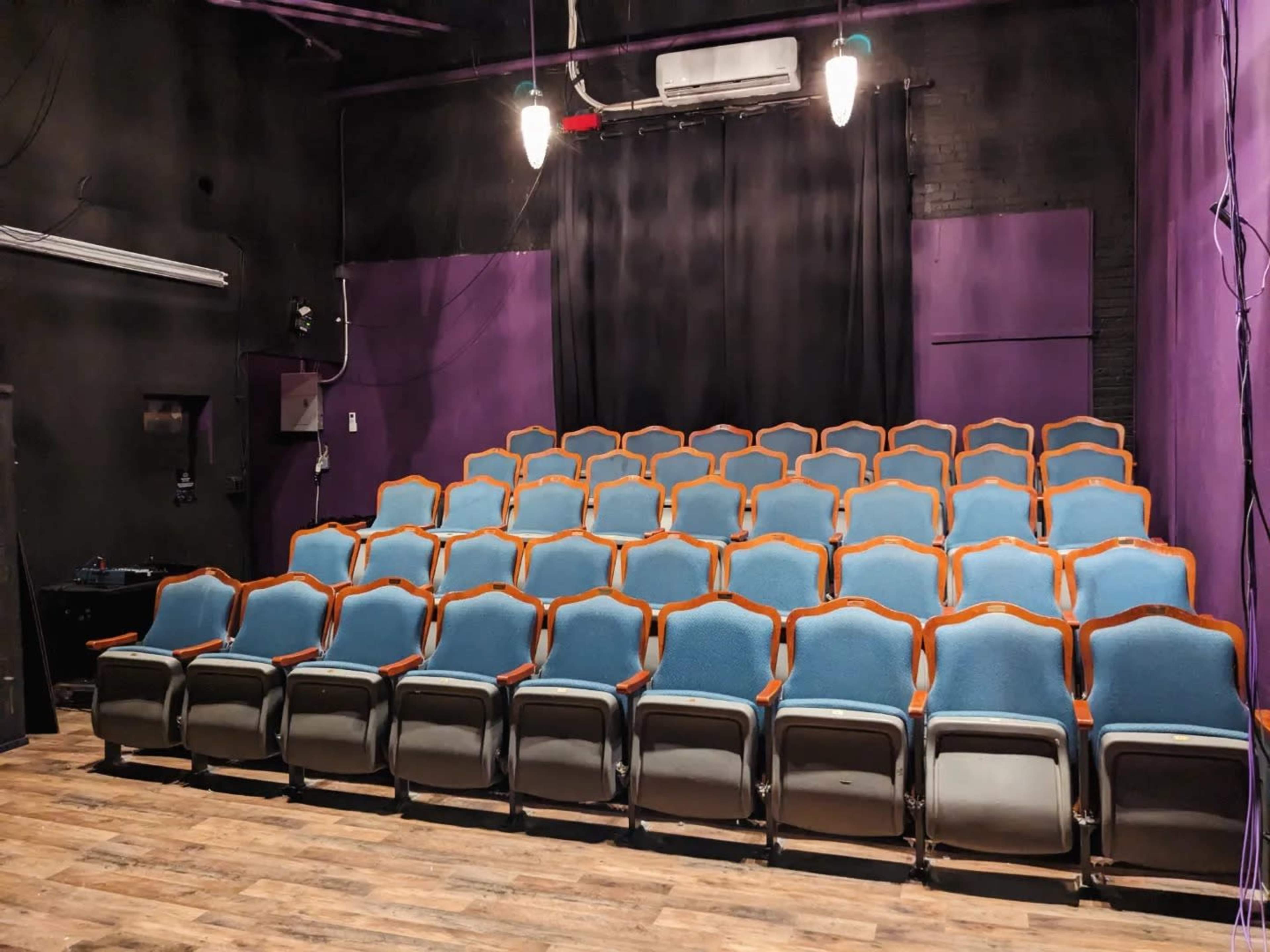A small theater with neatly arranged blue cushioned seats facing a black curtain in a purple-walled room.