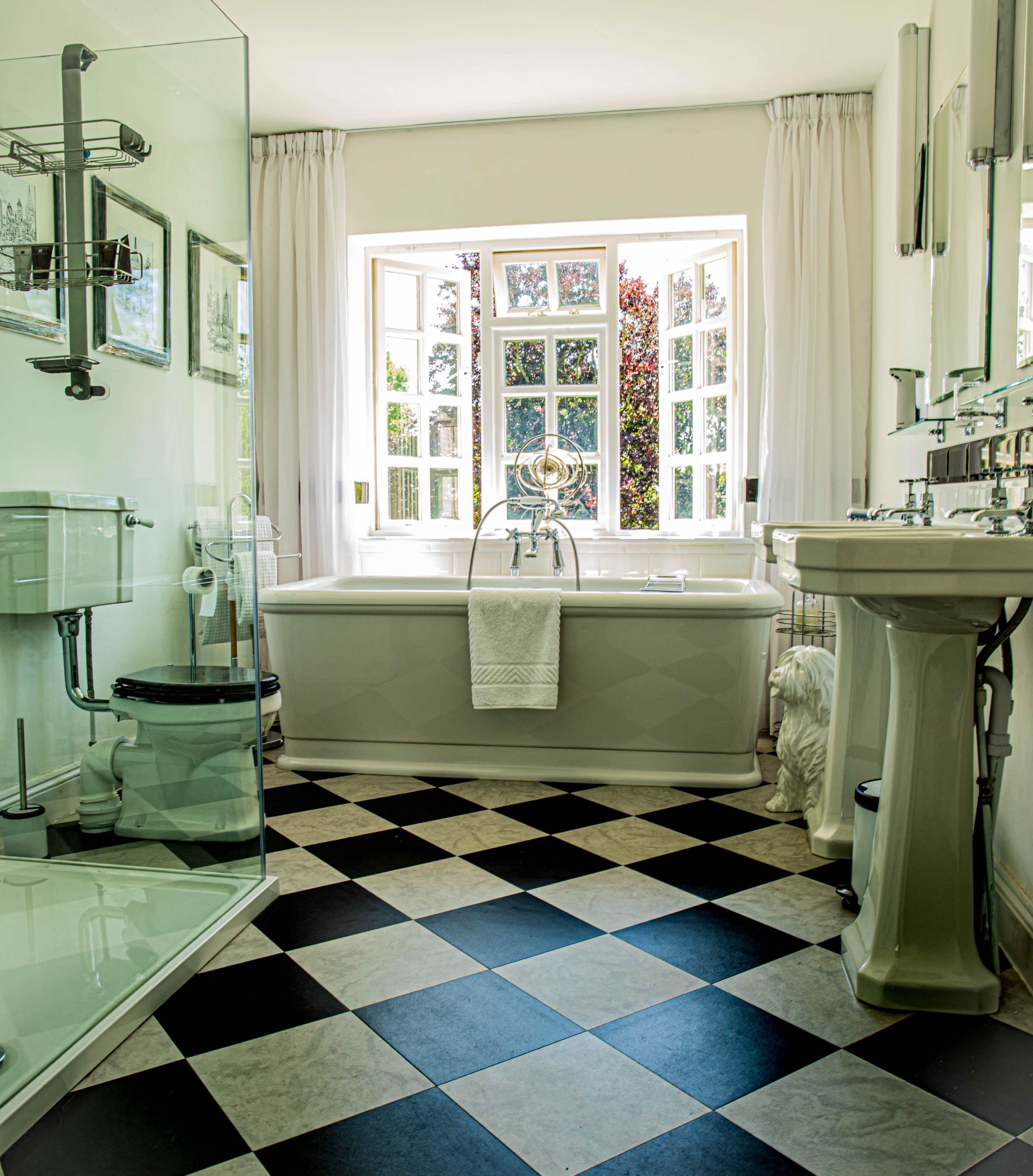 The bathroom features a freestanding bathtub, a glass-enclosed shower, and a window with multiple panes allowing natural light to fill the space.