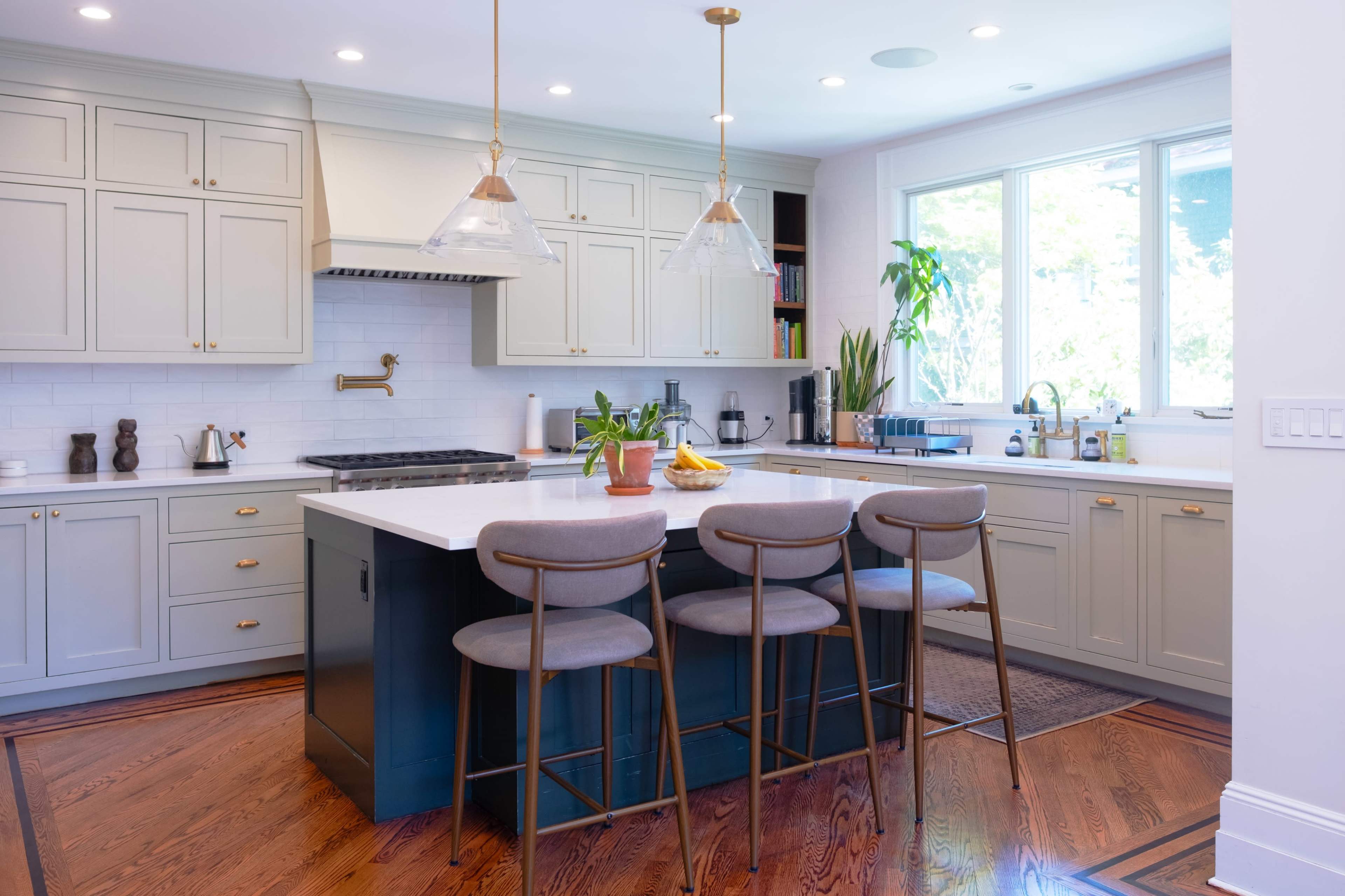The kitchen features light cabinetry, a large island with three stools, and a bright window that provides natural light.