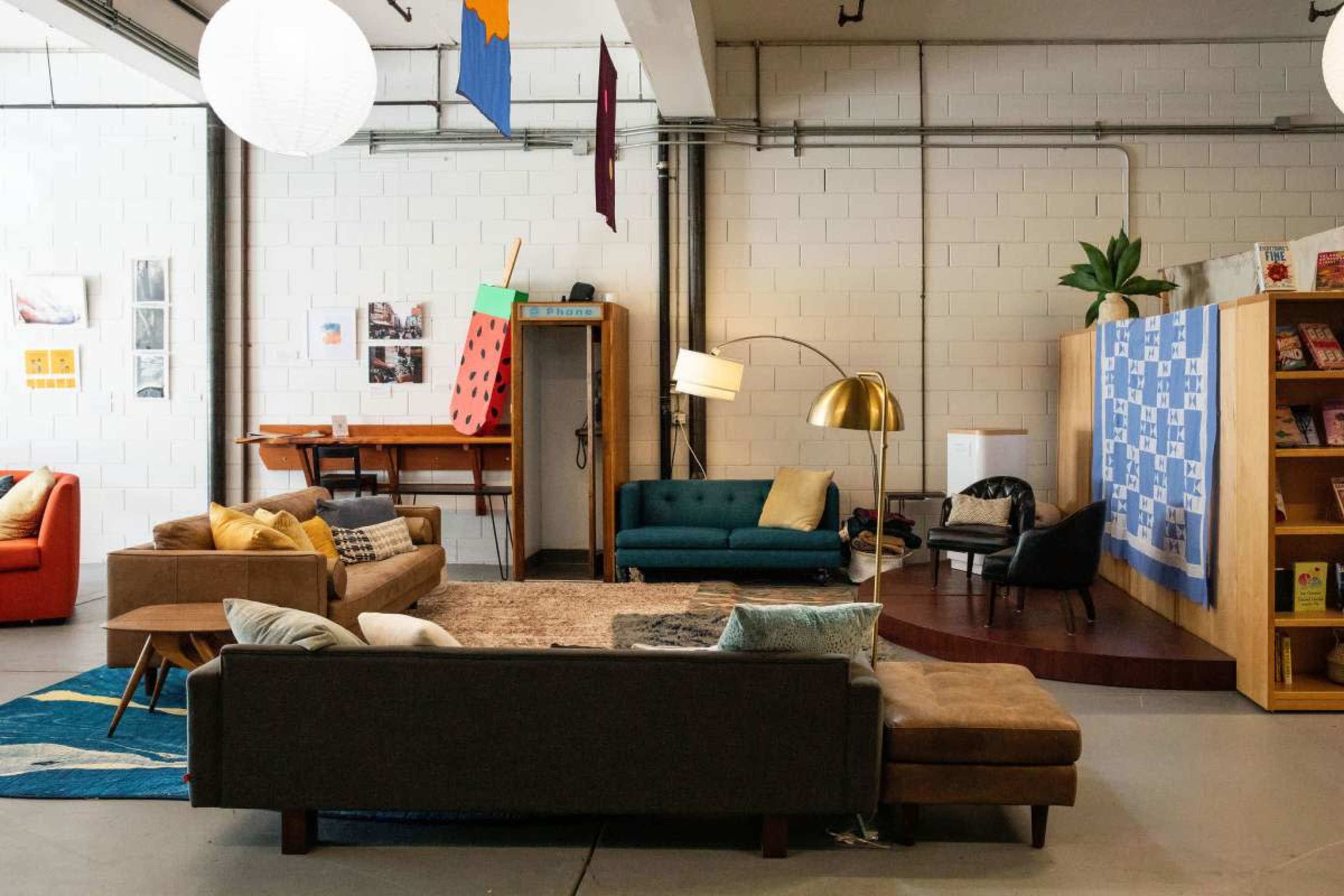 The image shows a spacious, modern indoor lounge area featuring various seating arrangements, a bookshelf, and decorative elements including wall art and plants.
