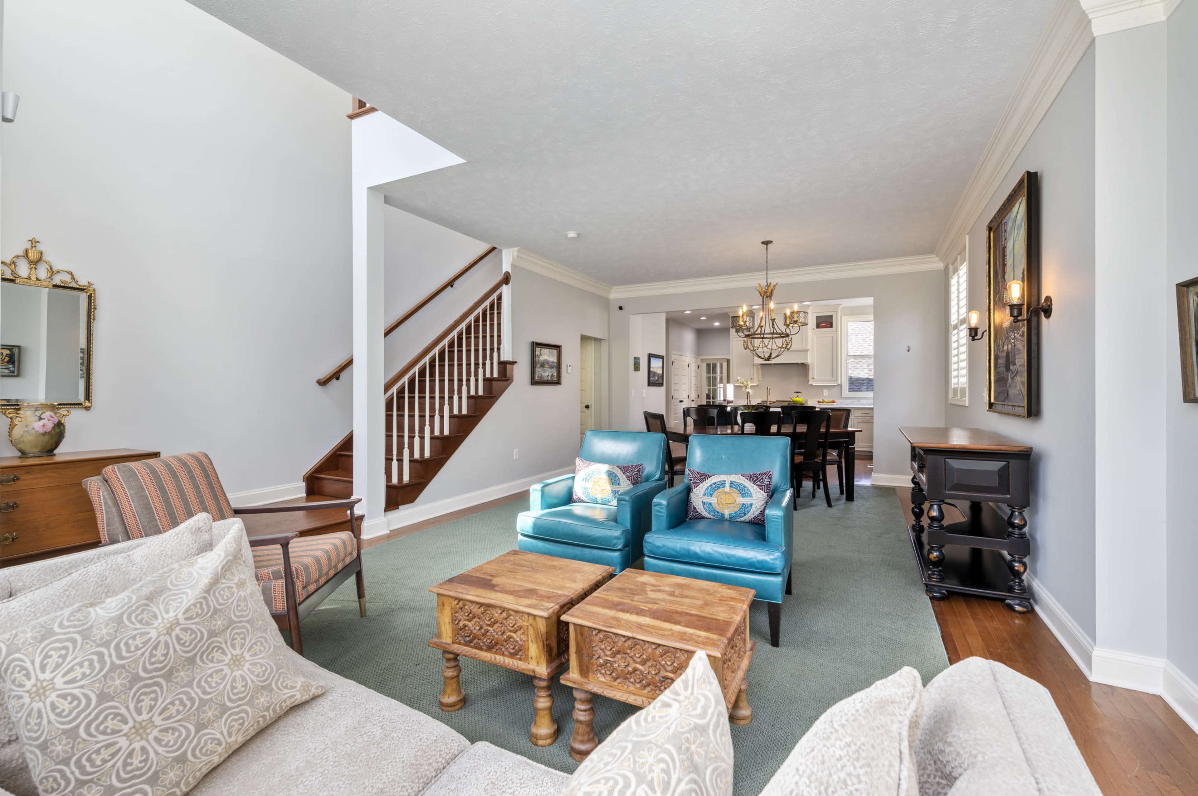 A spacious living area with teal armchairs, wooden coffee tables, and a staircase leading to the upper level.
