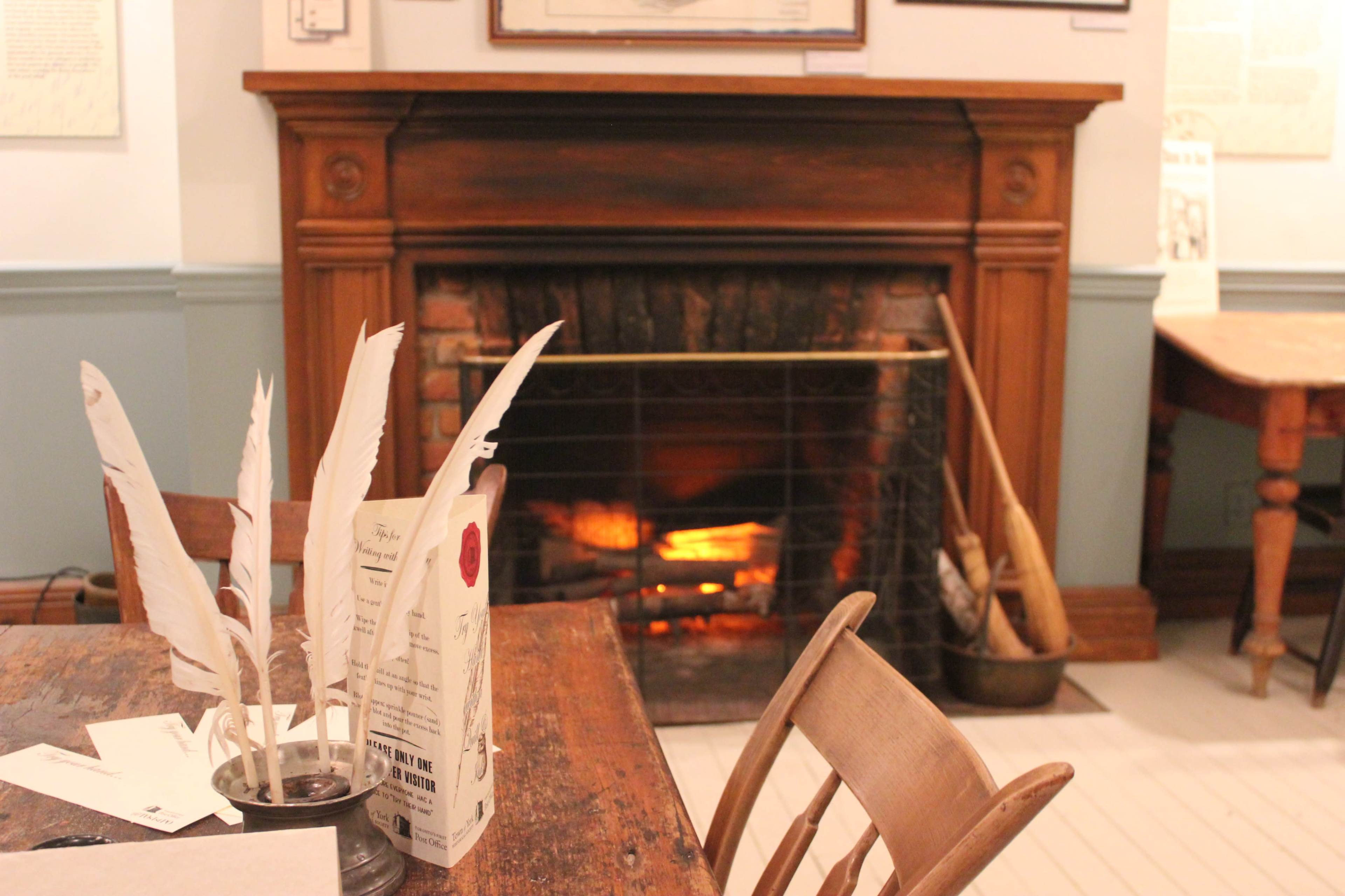 A cozy fireplace with a glowing flame is set against a wooden mantel in a room with rustic furniture and decorative items on the walls.